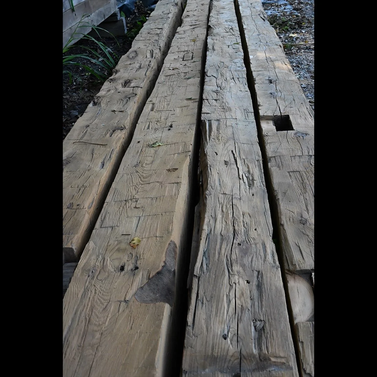 Antique reclaimed hand-hewn timbers with visible adze or broad axe marks, mortise pockets, and aged weathered patina.