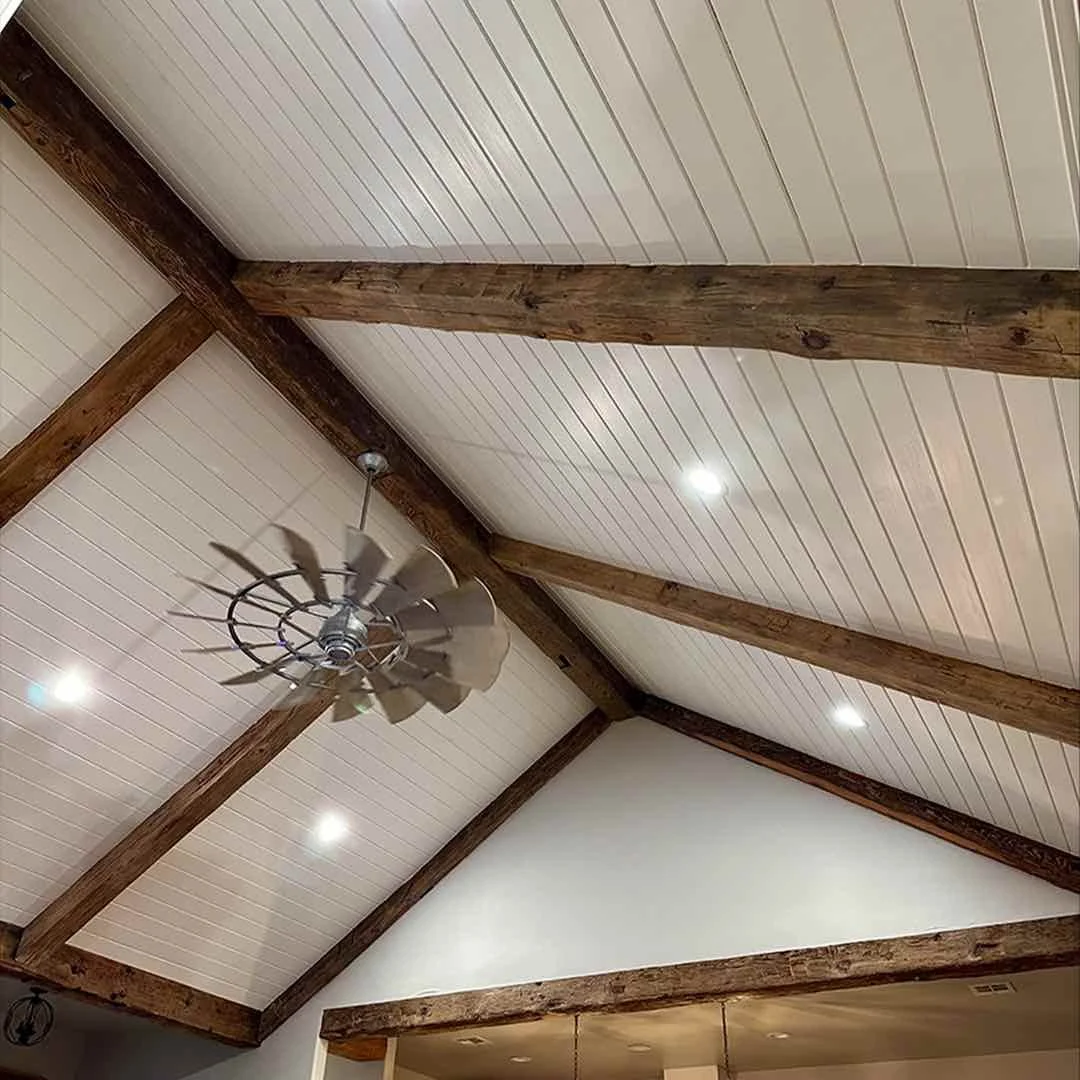 Antique reclaimed white pine ceiling beams in a client's home, showcased with a vaulted ceiling, farmhouse fan, and modern lighting.