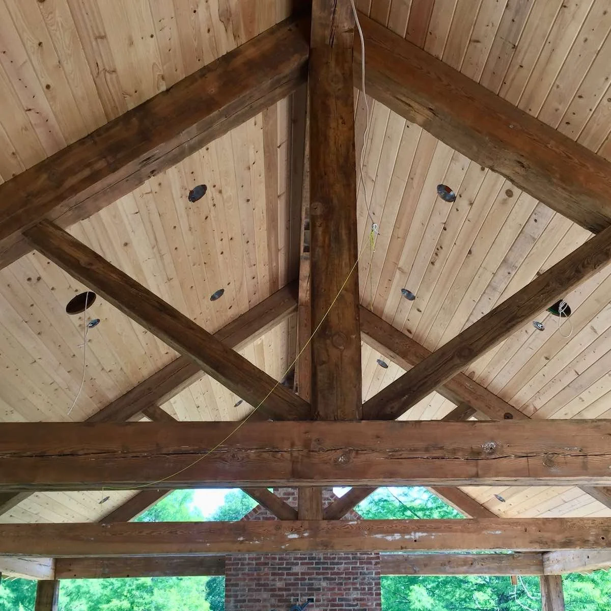 Reclaimed industrial timber truss ceiling  installation, featuring exposed antique beams with aged patina and light wood planking for rustic architectural character.