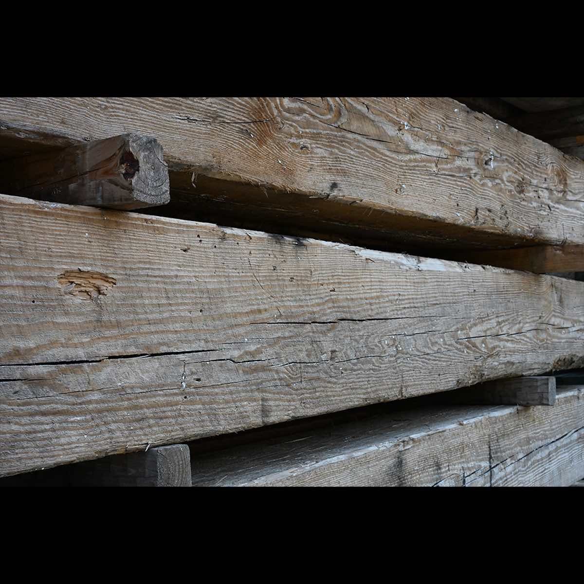 Close-up antique reclaimed industrial timbers stacked with visible grain, aged cracks, and natural patina.