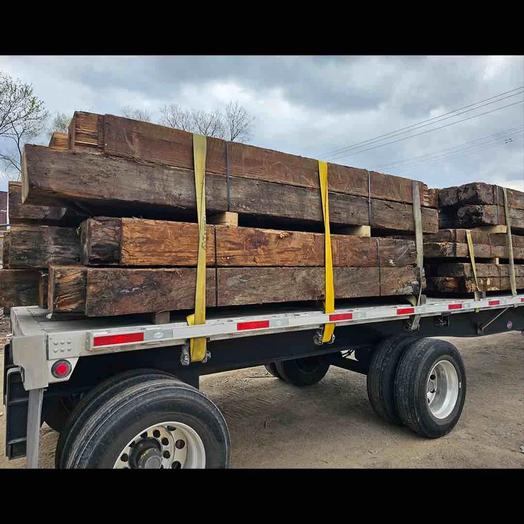 Thumbnail of antique reclaimed industrial  timbers stacked and secured with yellow straps on a flatbed trailer, showcasing salvaged old-growth lumber ready for transport.