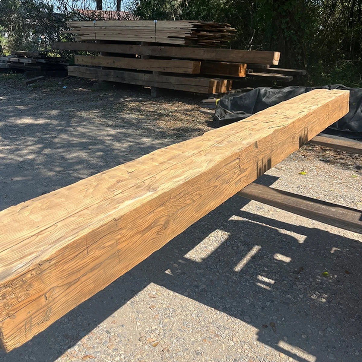 Long antique reclaimed hand-hewn timber with visible adze marks and natural grain, carried by forklift outdoors.