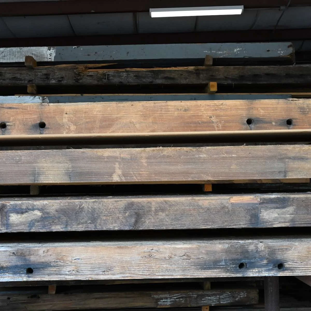 Stacked antique reclaimed industrial timbers with aged patina, weathered grain, and historic bolt holes.