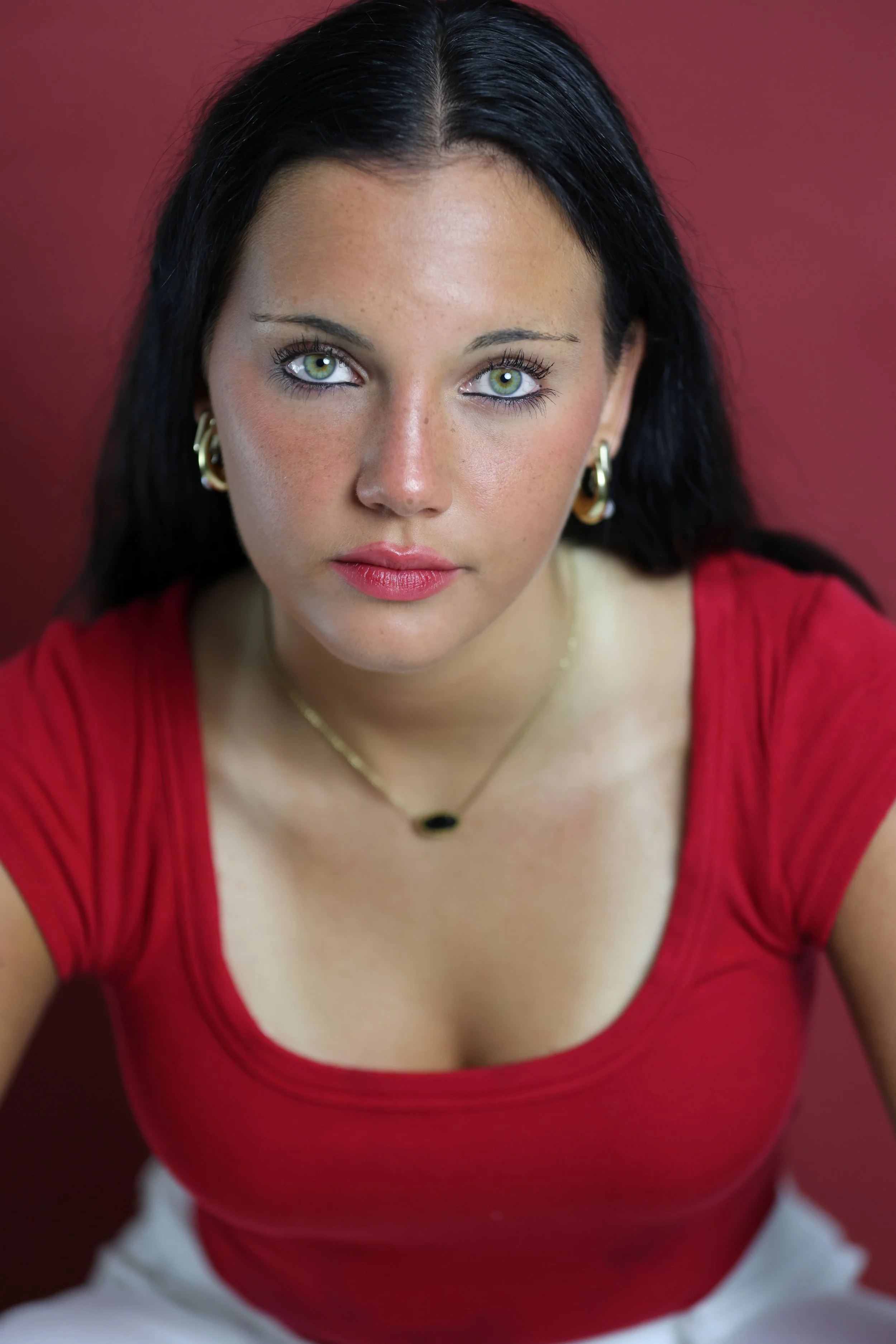 Close-up of a young woman with long dark hair and green eyes wearing a yellow sleeveless top against a green background.