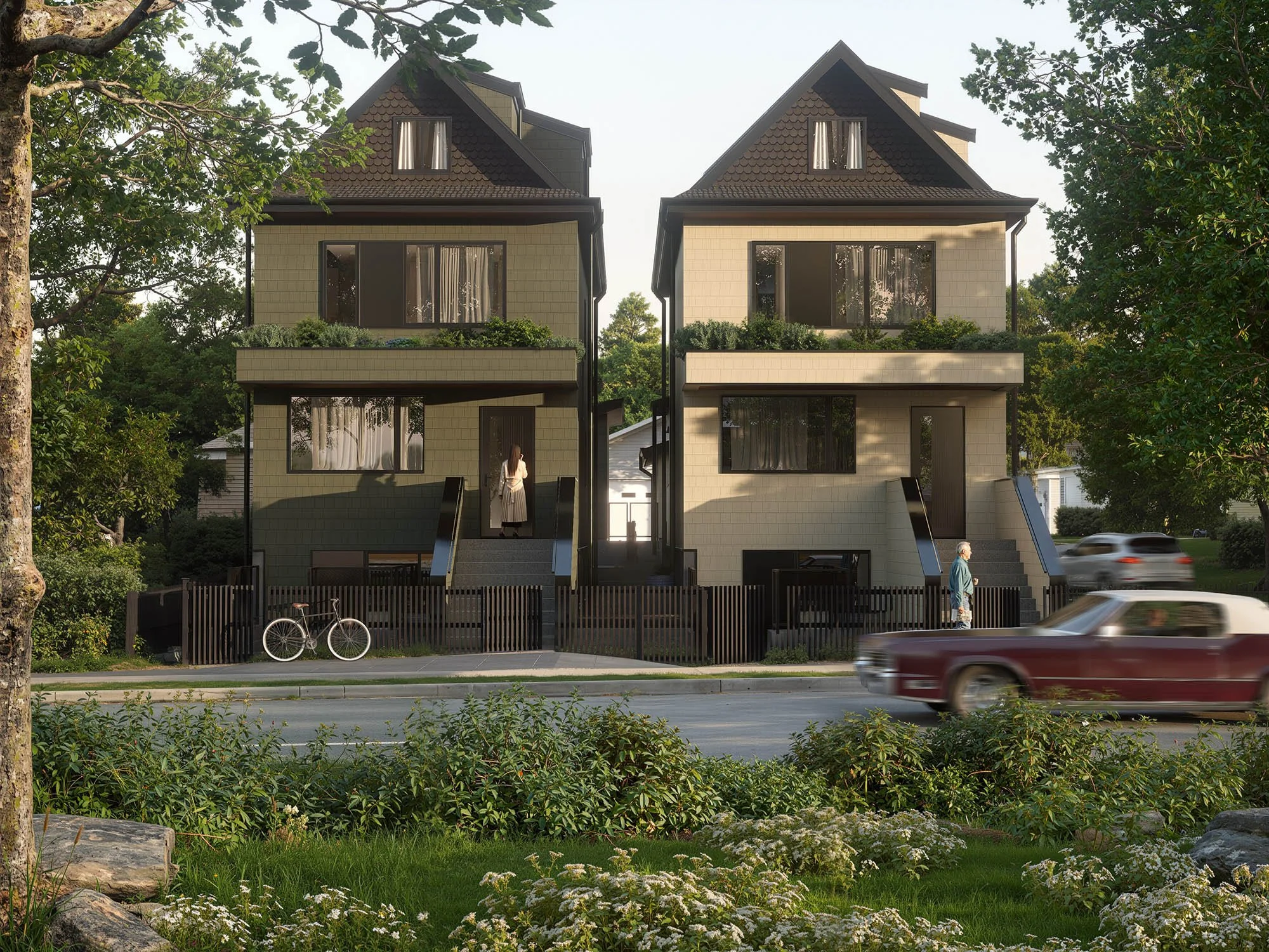 Two modern, multi-story houses side by side on a leafy street, with trees, shrubs, and flowers in the foreground, and cars passing by on the road.