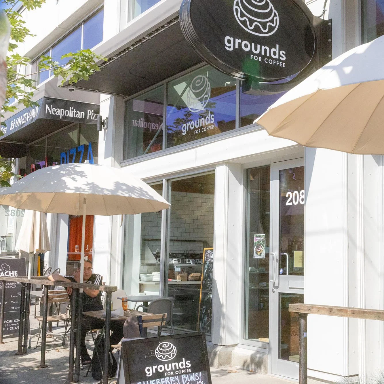 Exterior view of Grounds for Coffee shop with outdoor seating, umbrellas, and signage, located on a sunny street.