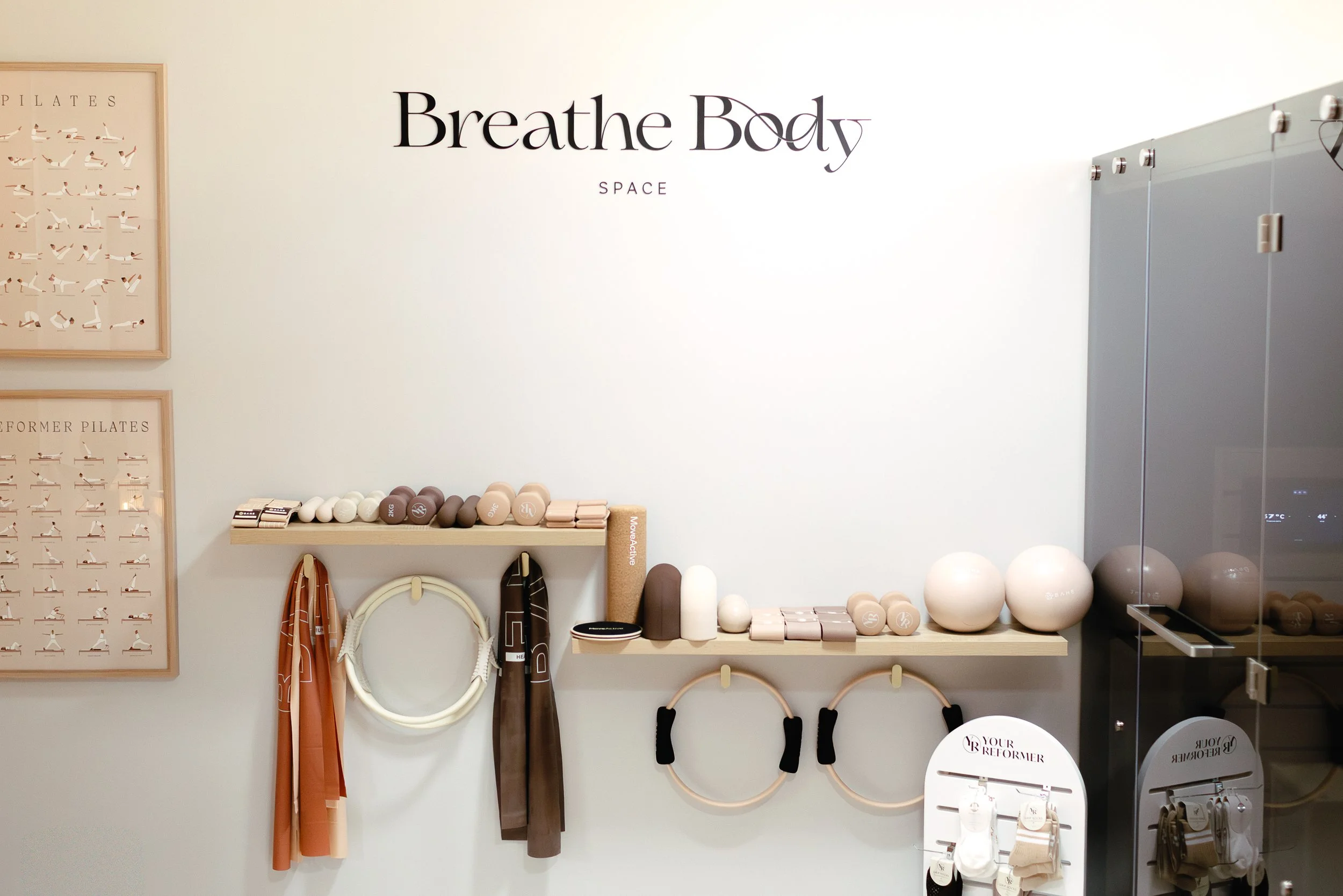 At home pilates studio wall with the words 'Breathe Body Space' and shelves with workout equipment like dumbbells, resistance bands, and exercise hoops.