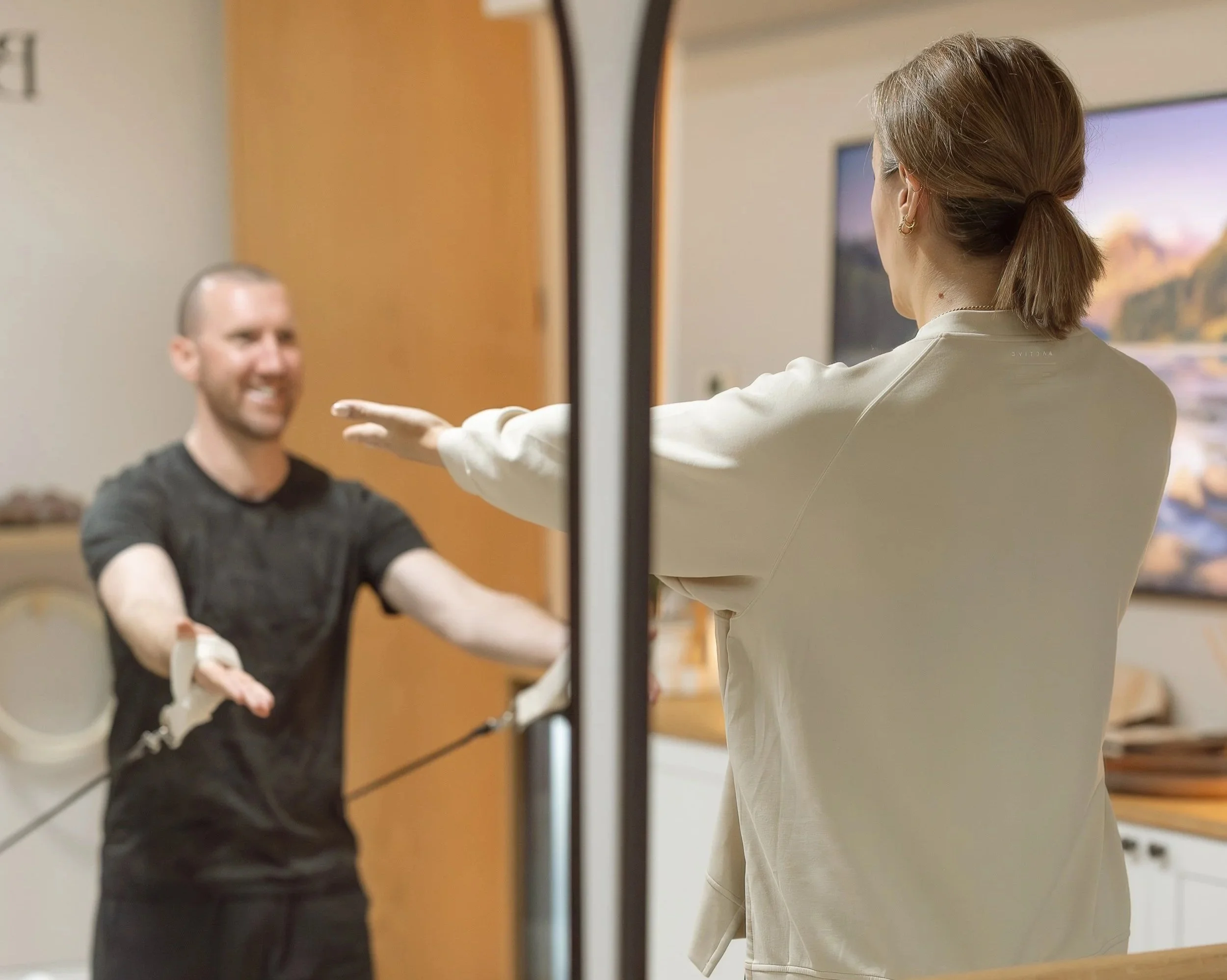 A man practising pilates on a reformer pilates machine, being taught by a female pilates teacher.