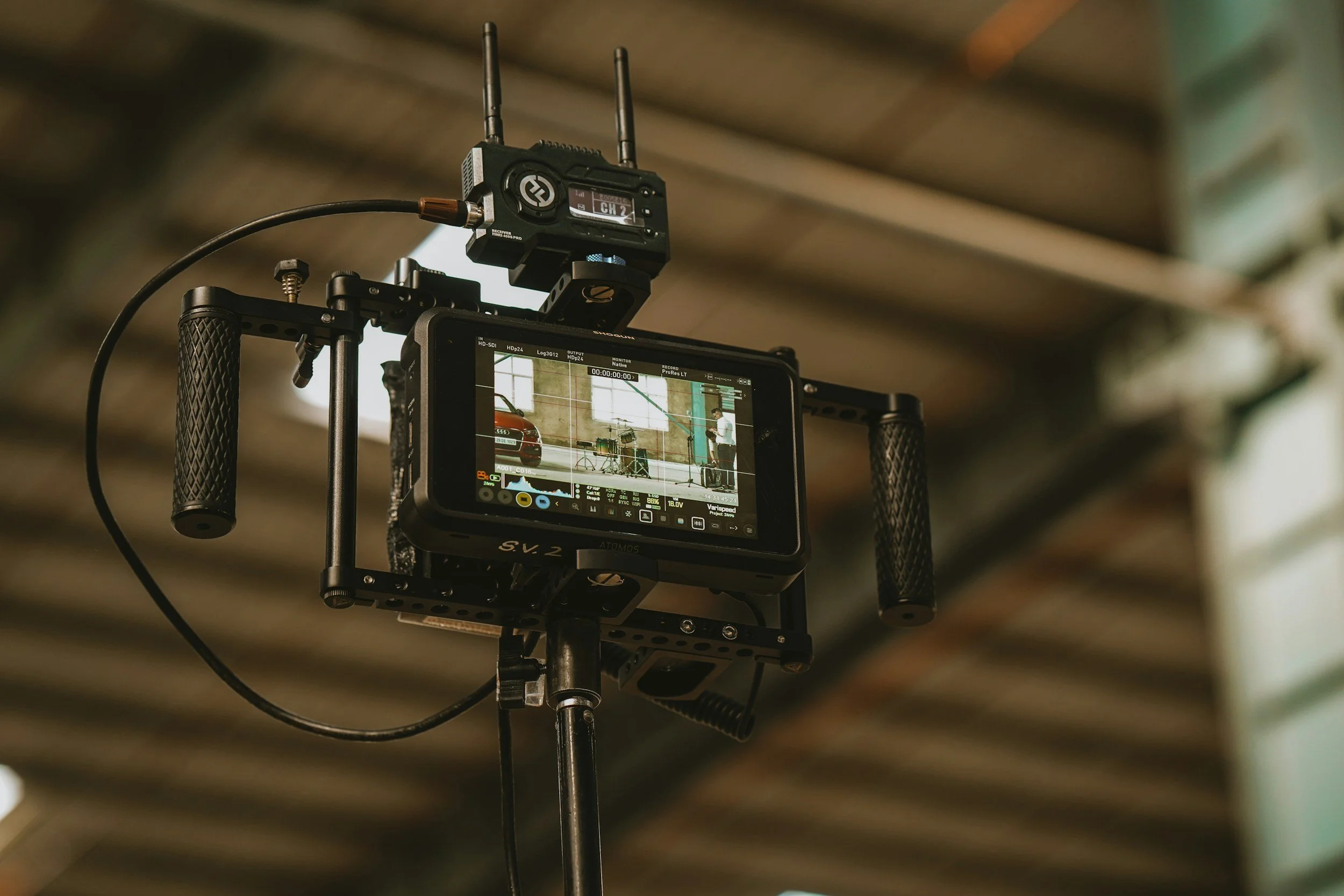A professional video camera setup on a tripod, with a monitor displaying a scene involving a person and some equipment indoors.