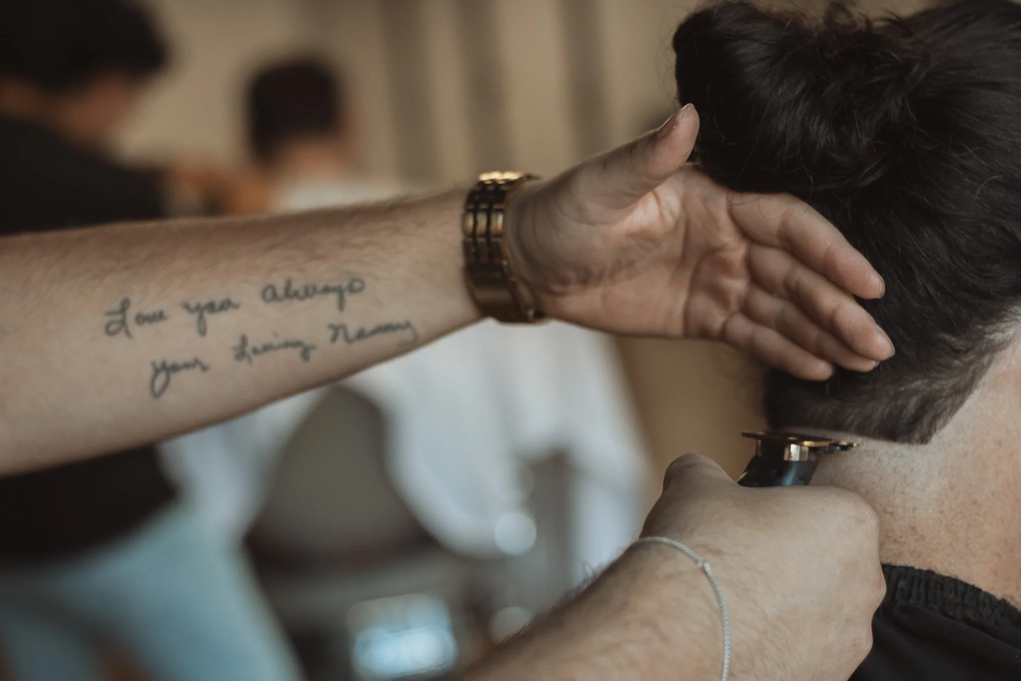 A person with tattoos and a bracelet is holding a stethoscope to another person's neck while touching their head, in a medical setting.