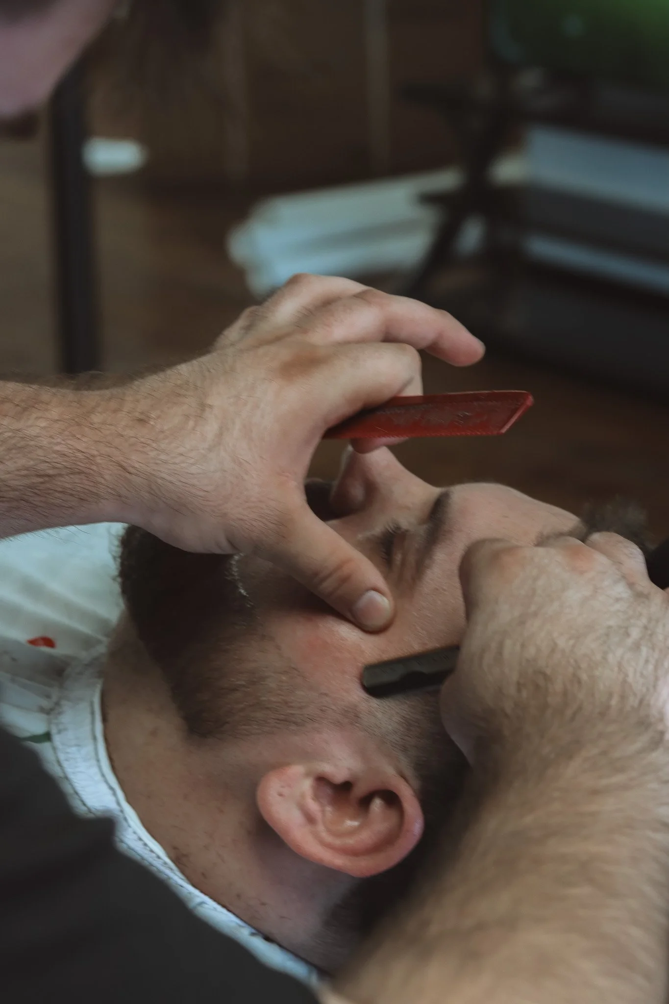 A man is lying down with eyes closed while another person performs an eye examination using a flashlight and an optical device.