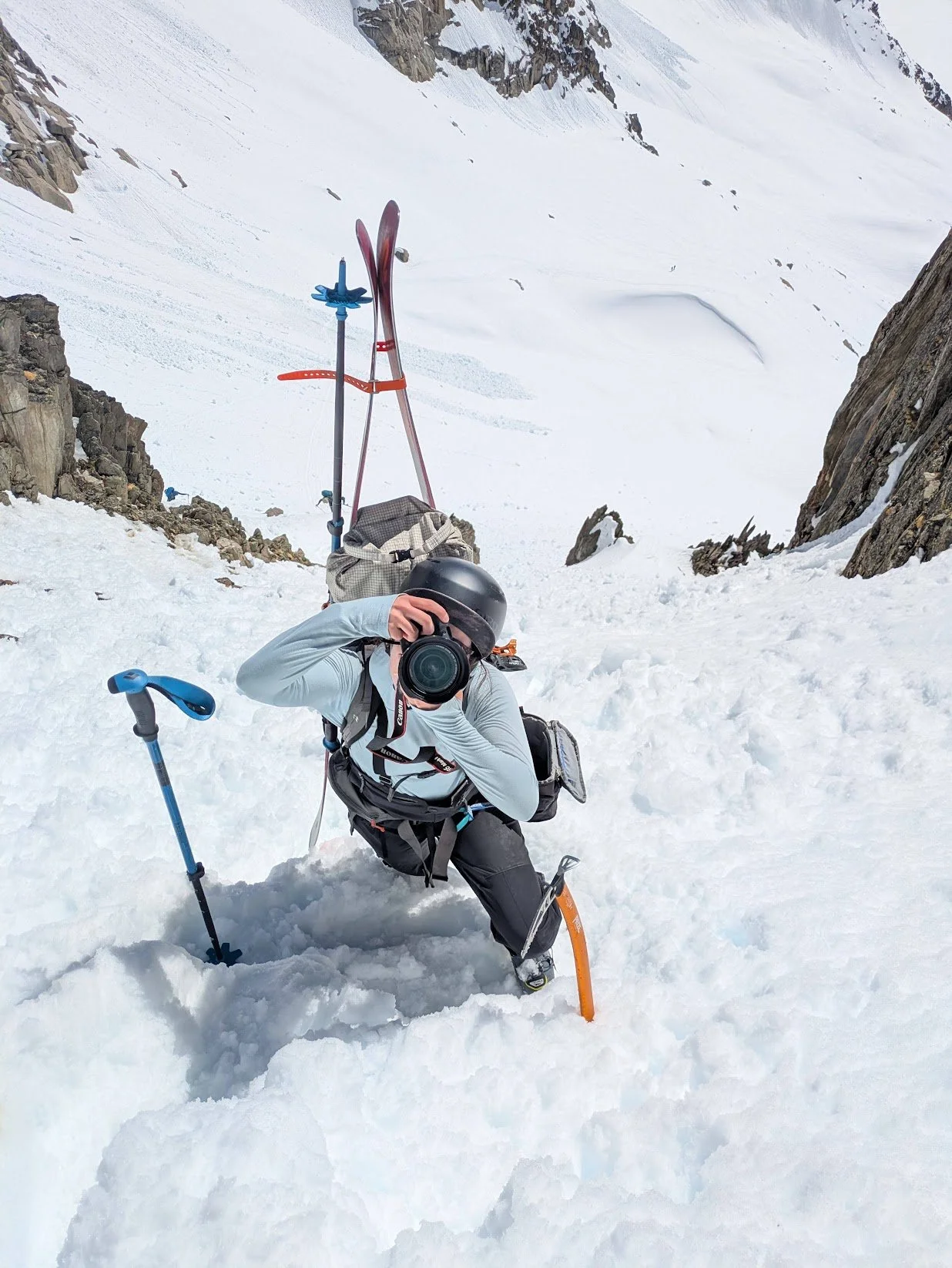 Amelia DiGiano photographs with her skis on her back in a steep couloir