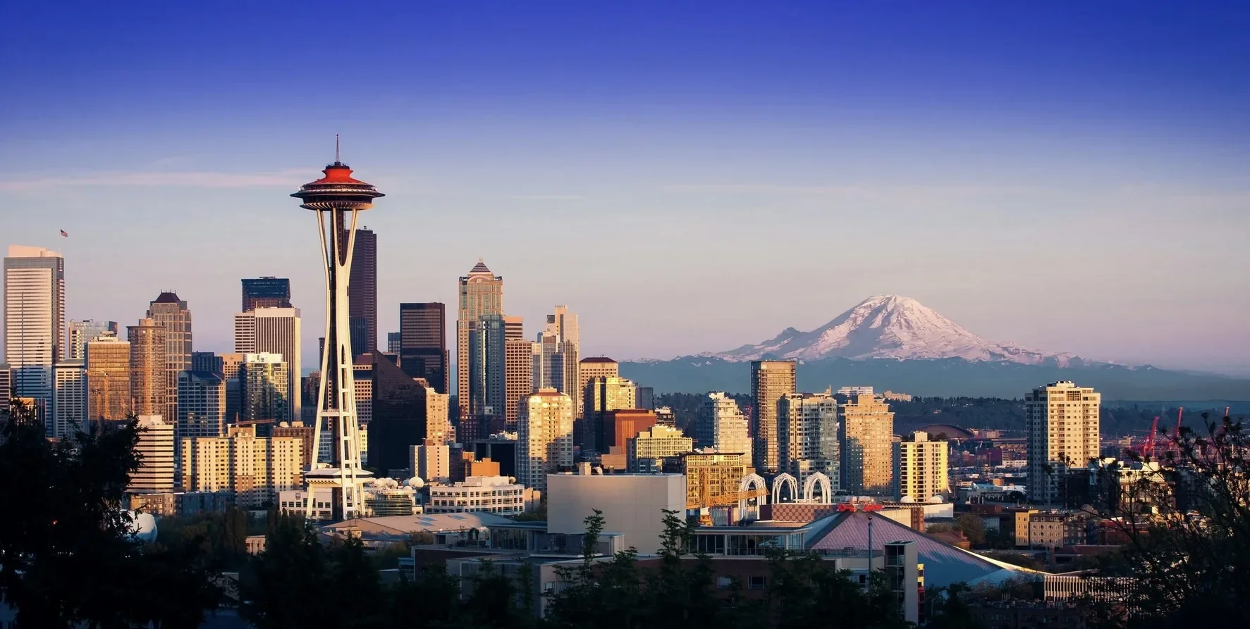 Seattle skyline featuring the Space Needle with Mount Rainier snow-capped in the background during sunset.