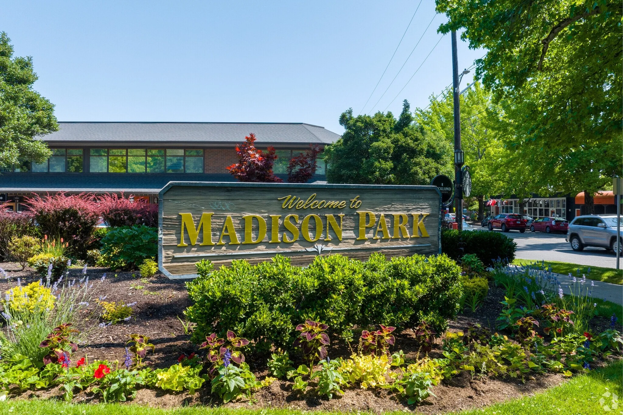 Welcome sign for Madison Park surrounded by colorful flowers and lush green bushes on a sunny day.