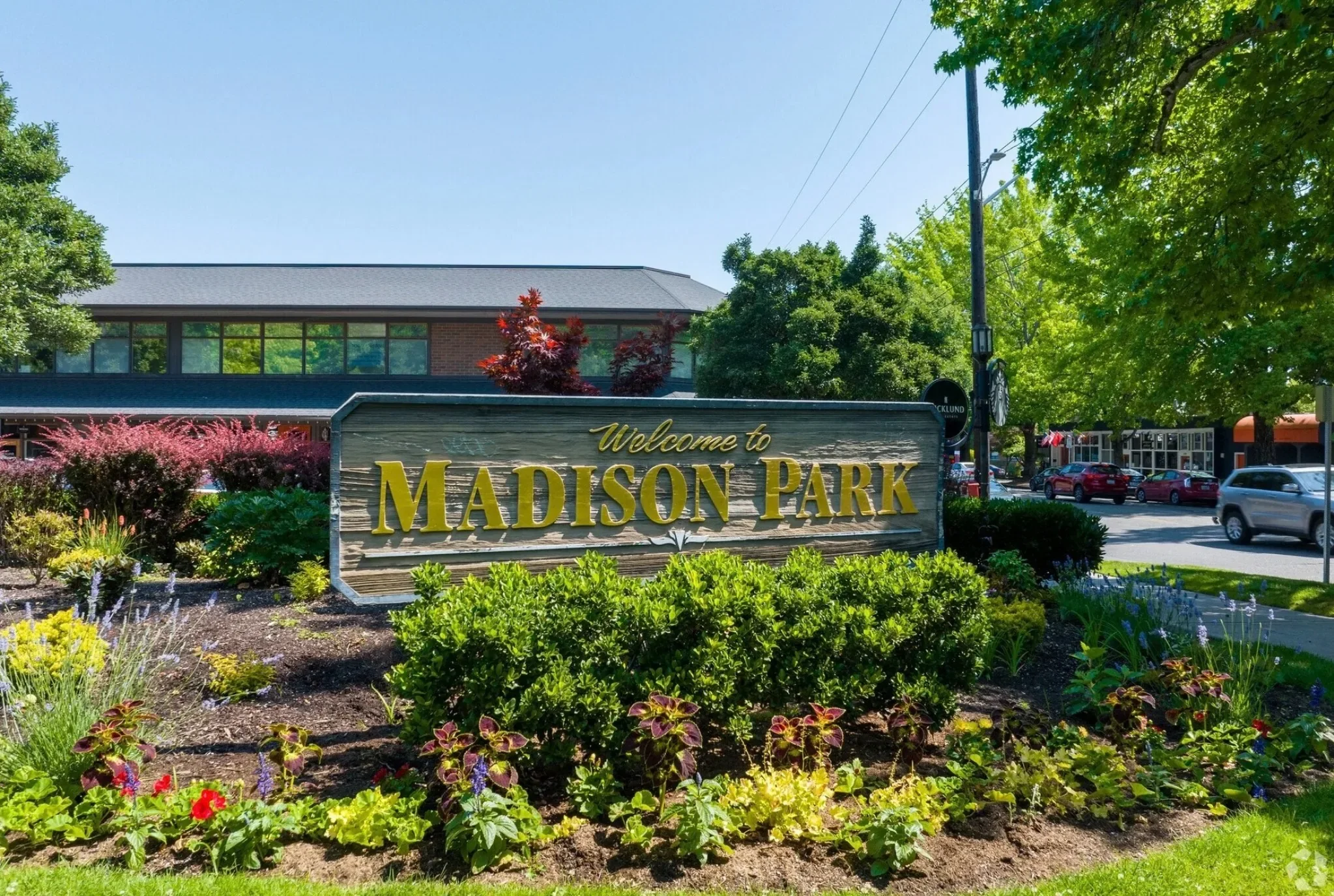 Welcome sign for Madison Park surrounded by colorful flowers and lush green bushes on a sunny day.