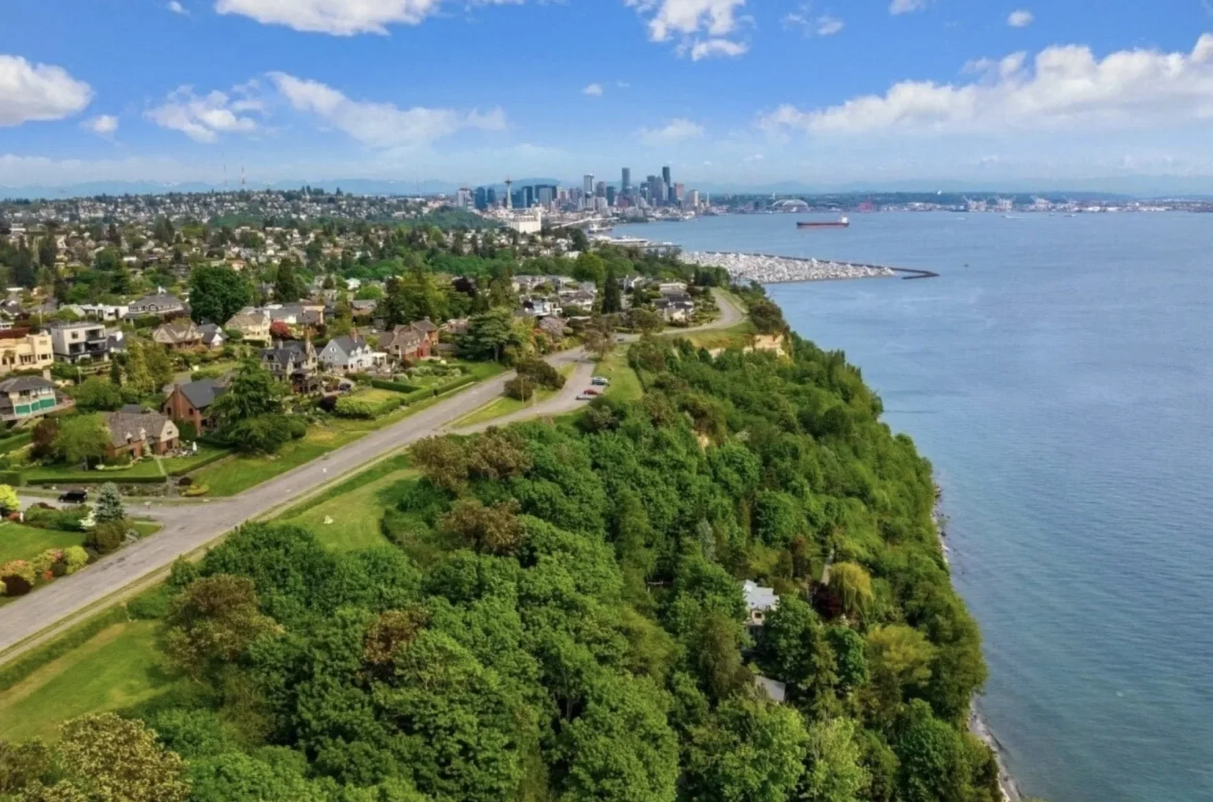 Aerial view of Seattle skyline with residential area, green trees, and waterfront with ships.