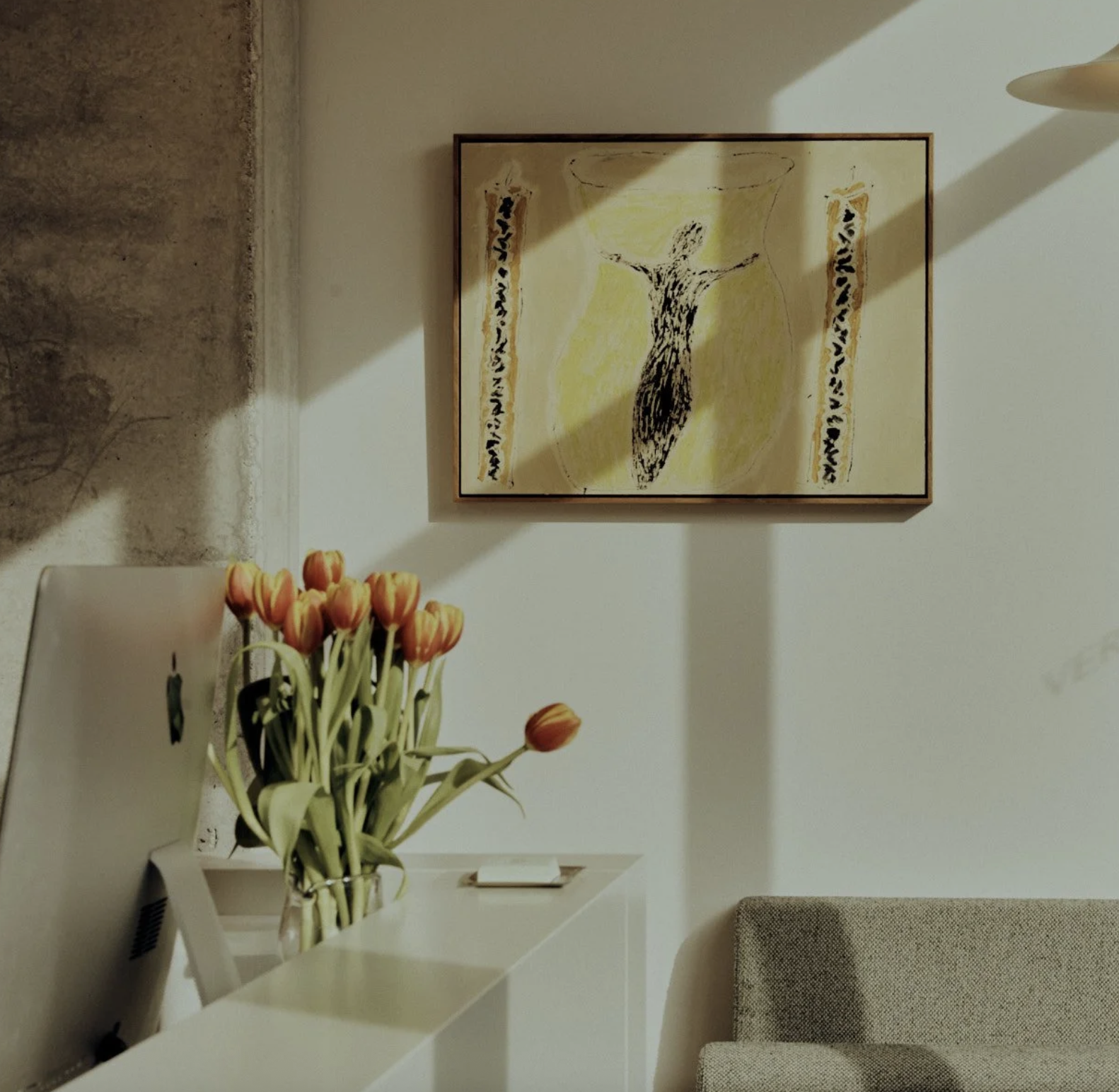 Living room with a framed abstract painting, a vase of orange tulips on a white side table, a patterned armchair, and a textured wall.