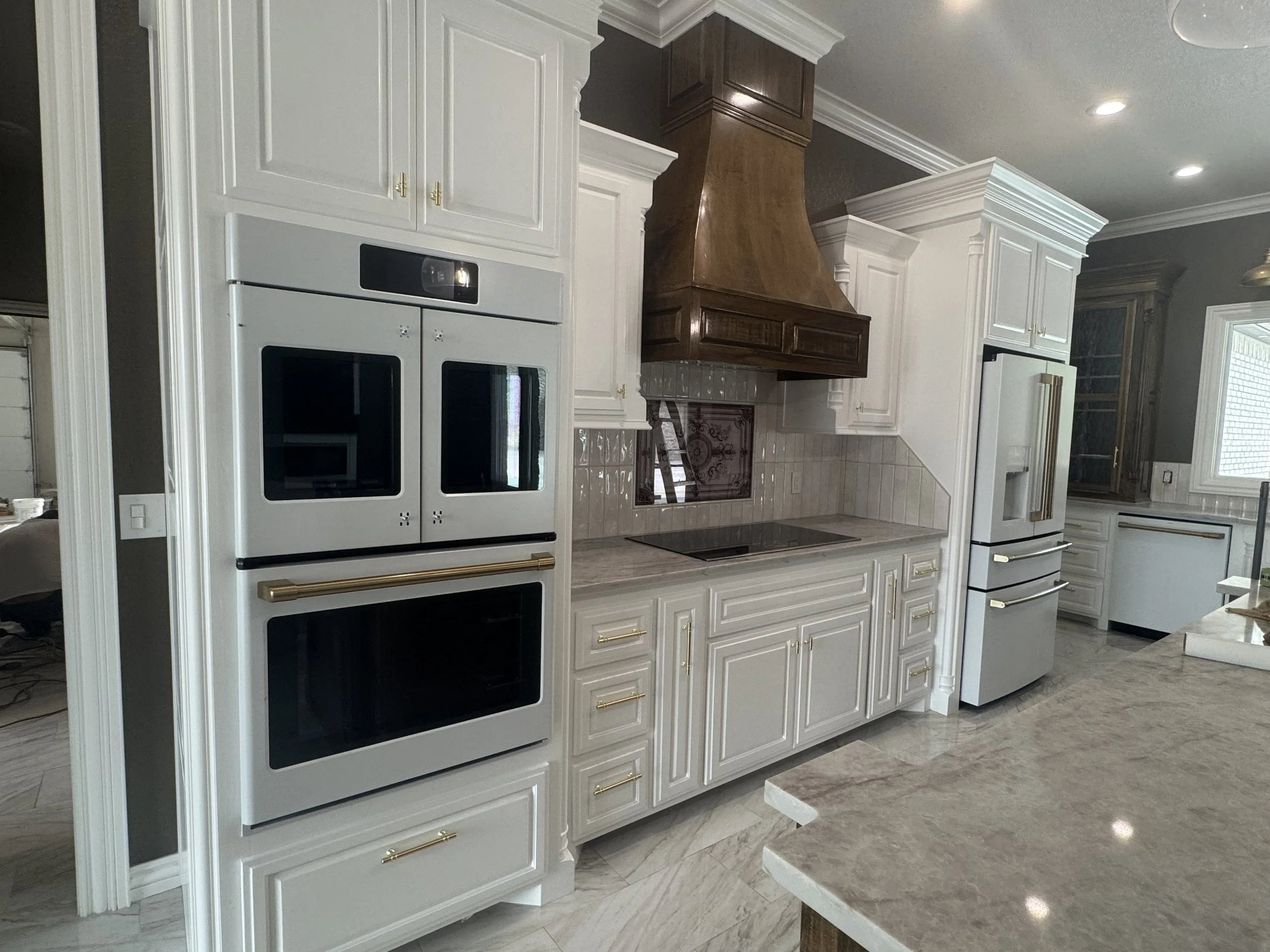 Clean residential kitchen with white cabinetry, built-in ovens, decorative range hood, and polished countertops.