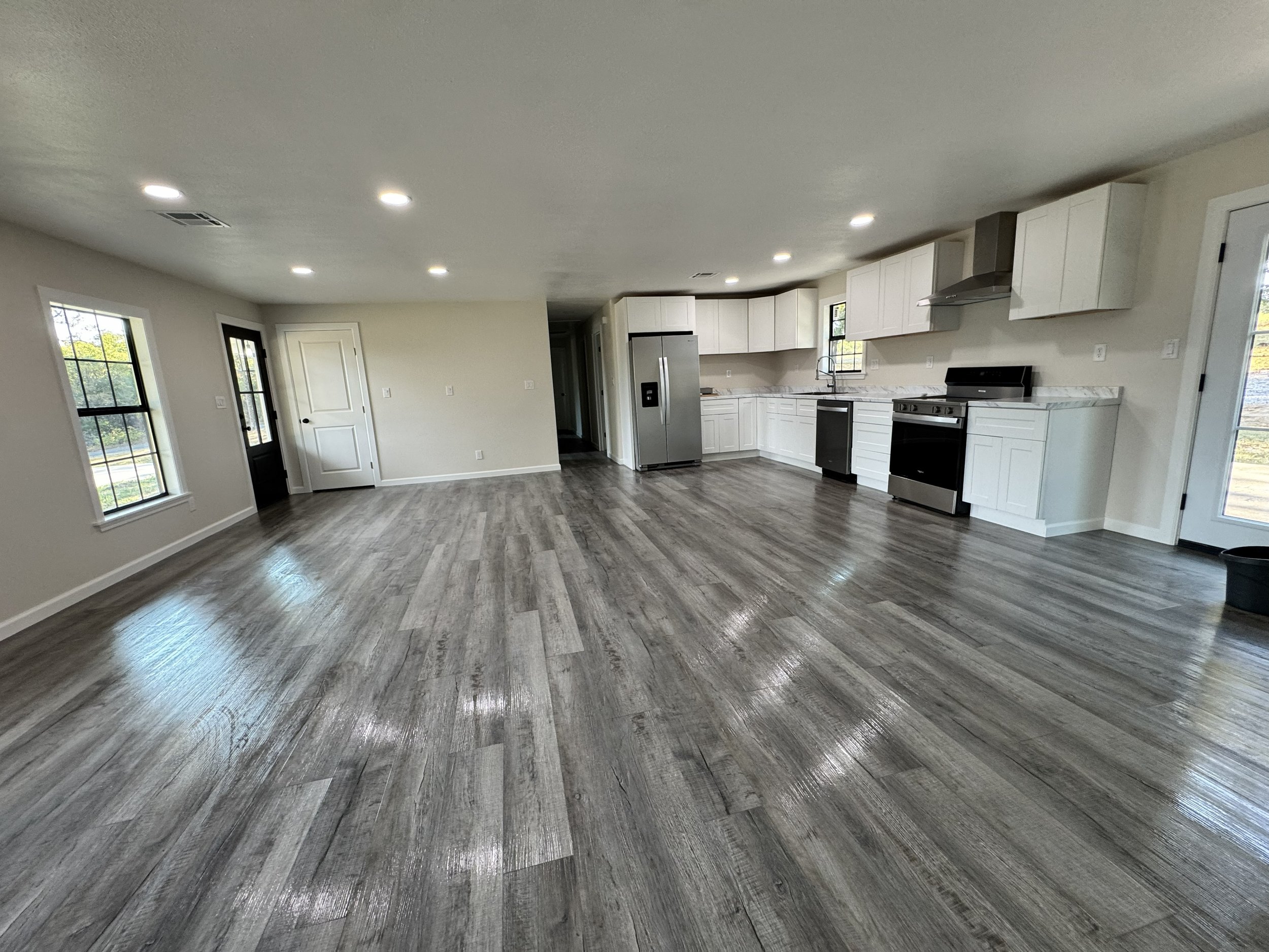 Clean, empty open-concept home with wood-look flooring, recessed lighting, and kitchen ready for new occupants.