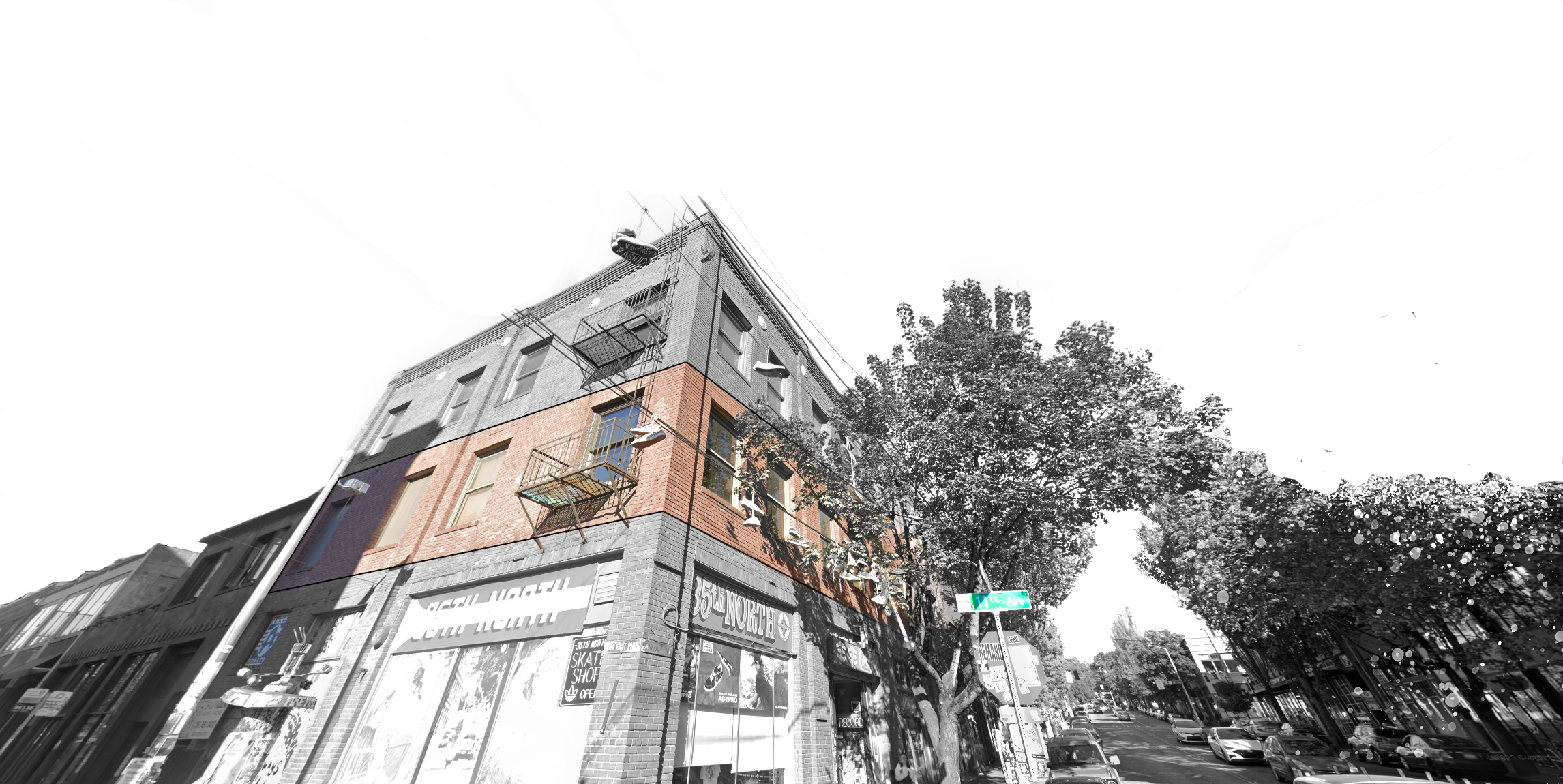 A picture of the Annex Theatre building, featuring signs and storefronts, with a tree-lined street and cars parked along the curb. The image is grayscale besides the second floor, which is in full color, showing the red brick.