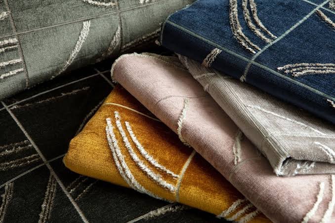 Stack of luxury folded designer fabric samples with various geometric fringe colors and patterns.