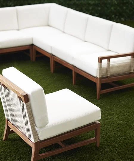 Outdoor designer Palecek white sectional sofa with high quality teak wooden frame and rope woven detail on a green lawn. Beautiful modern exterior furniture.