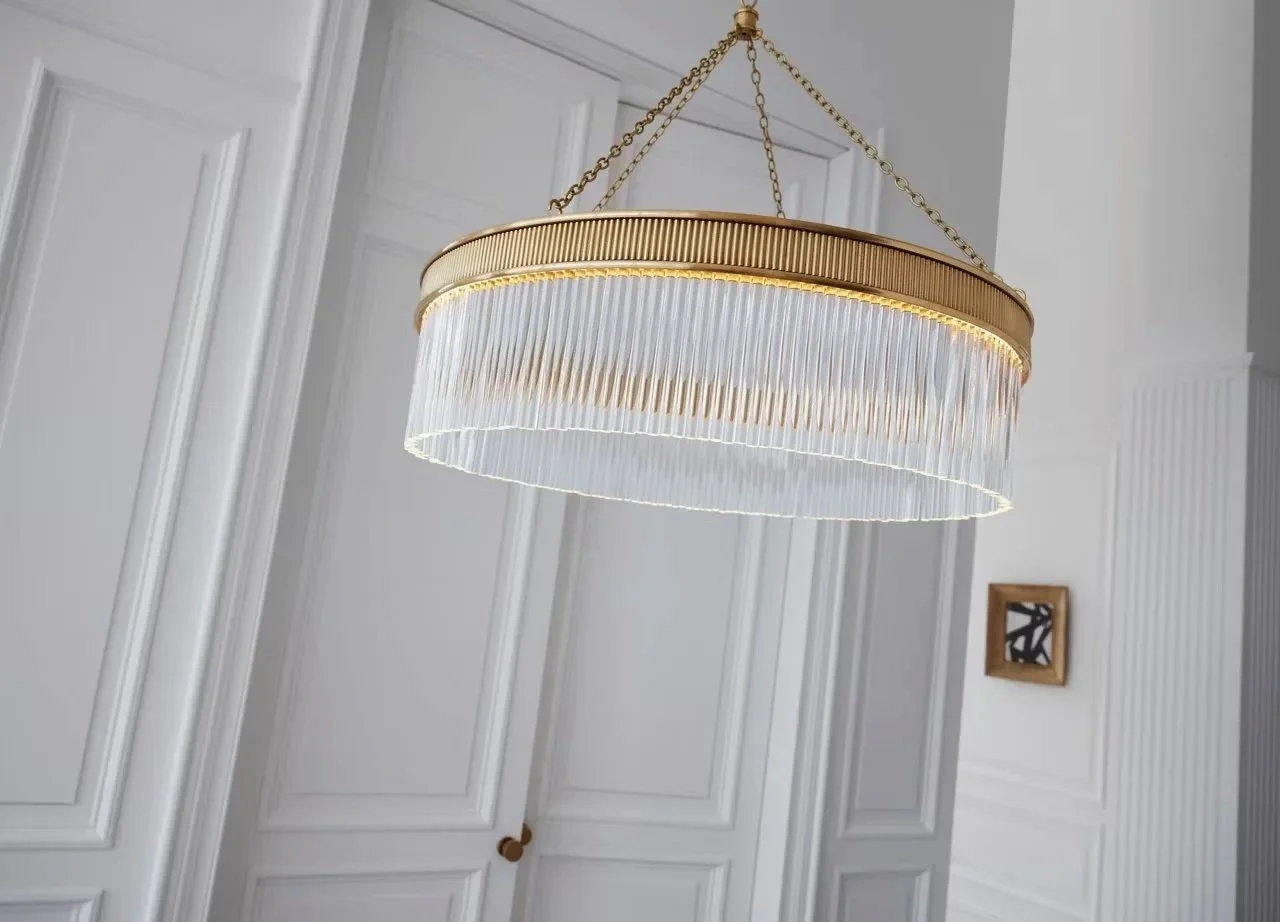 A Visual Comfort designer modern ring chandelier with glass rods and a gold brass frame hanging from three gold chains in a white traditional room.