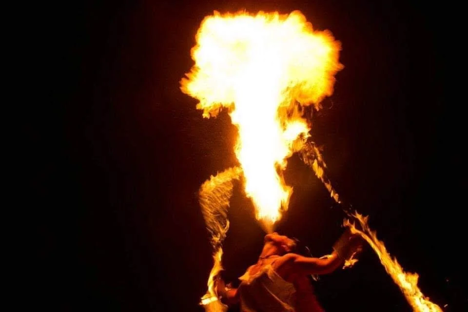 Fire performer spews a large flame into the air at night.