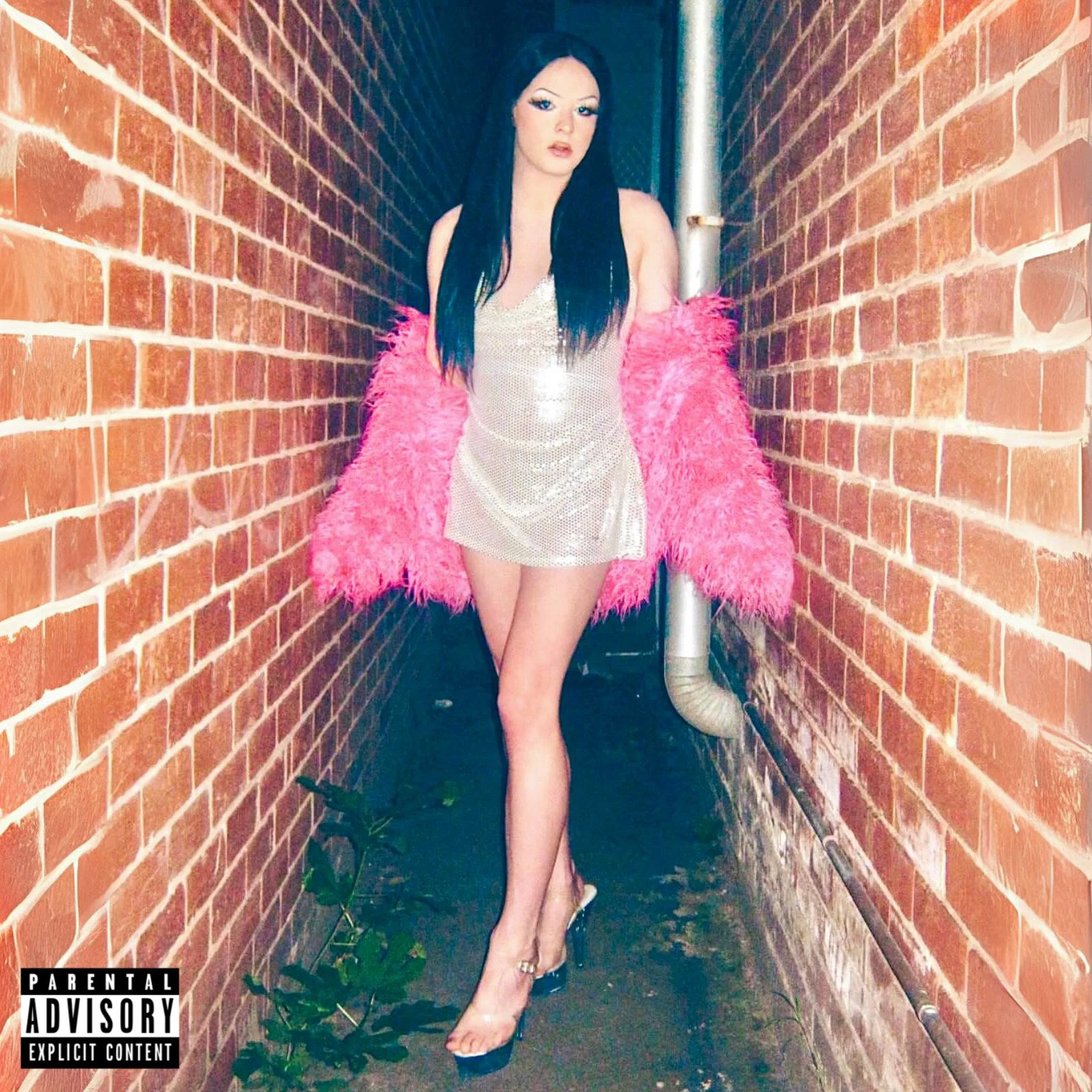 A woman with long dark hair and makeup stands in a narrow alleyway between brick walls, wearing a shiny silver dress, pink feathered jacket, and high heels.