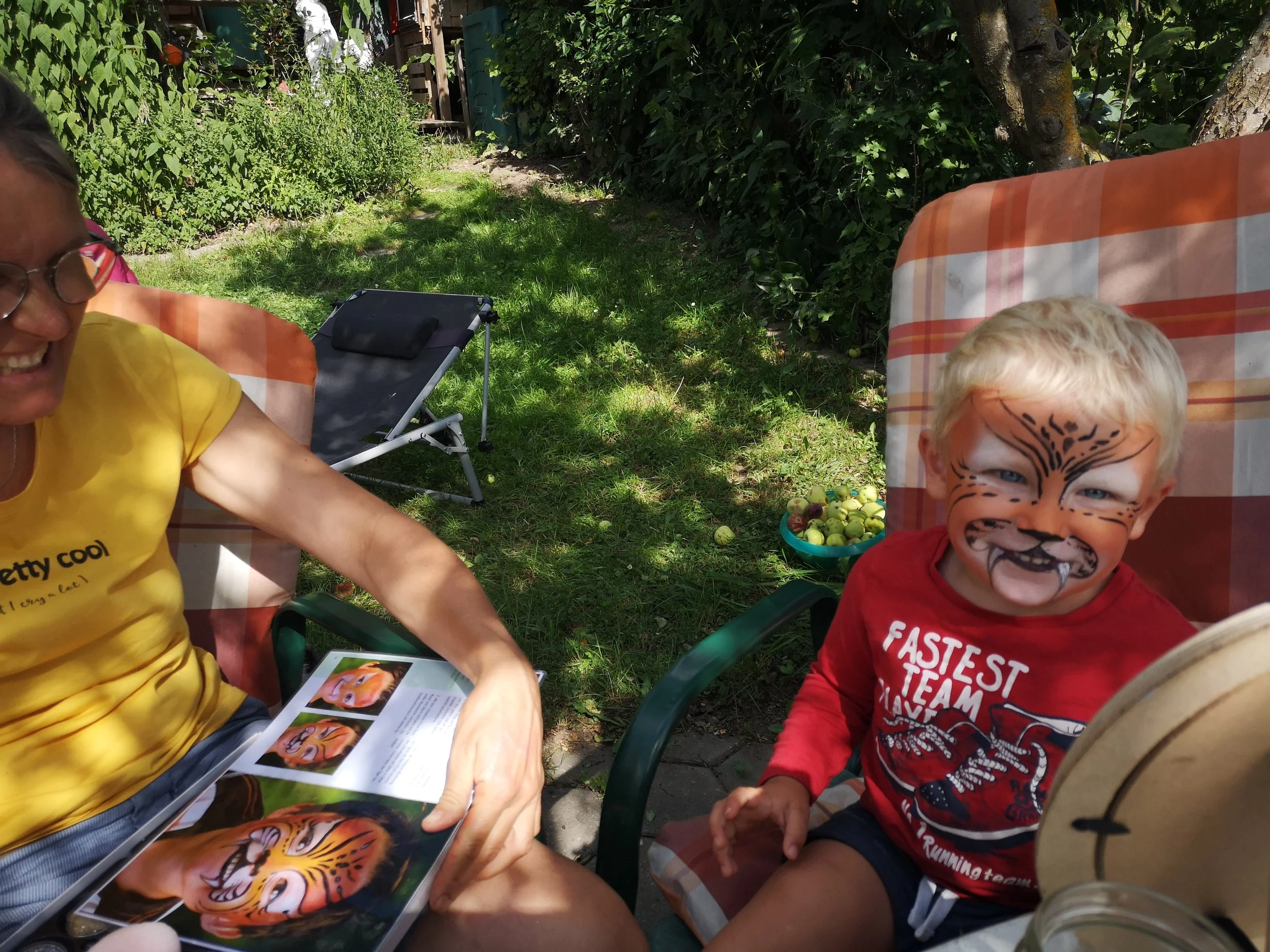 Ein Bub mit Gesicht bemalt, das wie ein Tiger aussieht, sitzt in einem Garten.