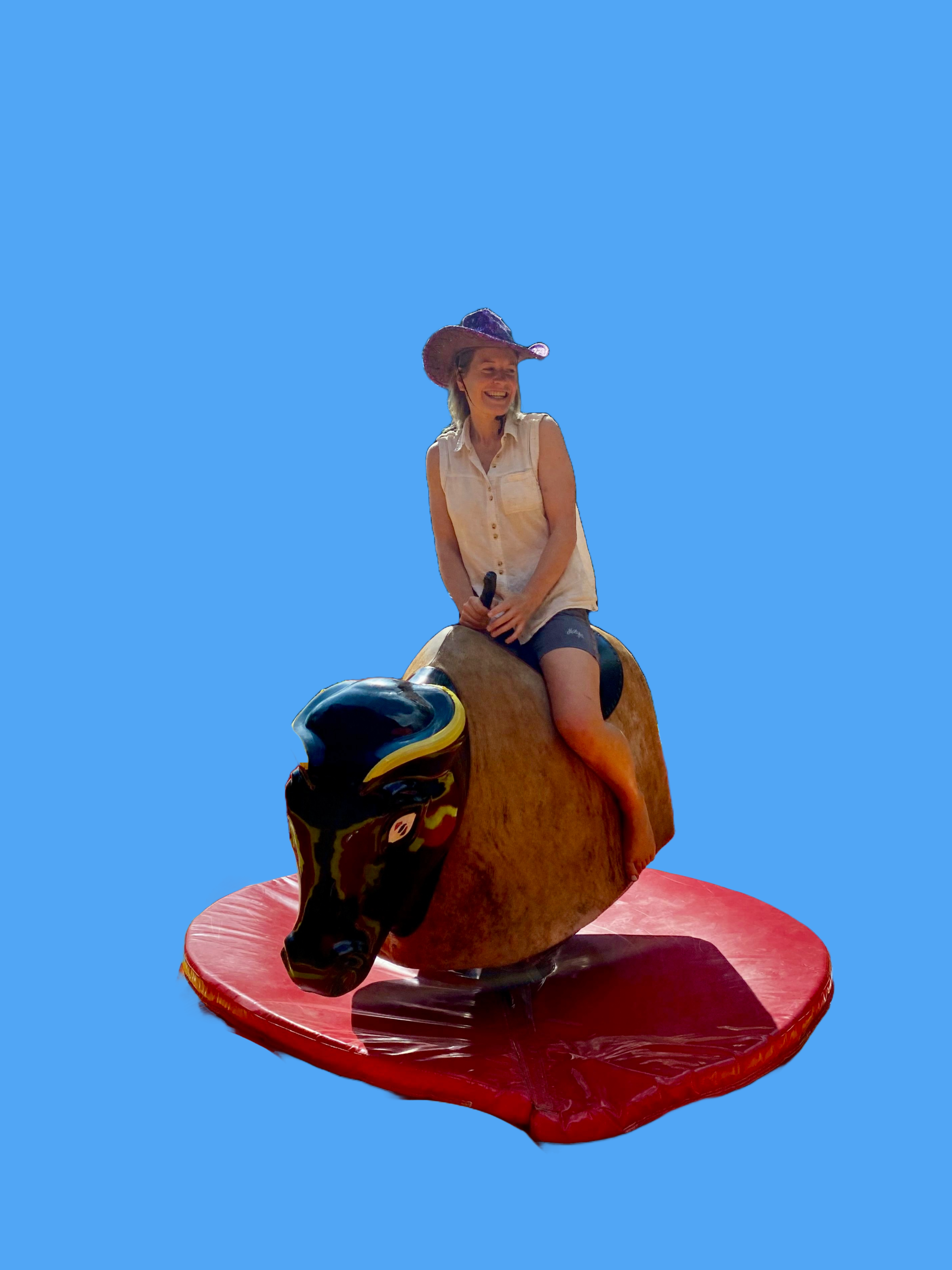 Frau sitzt lachend auf einem Rodeo Bulle mit Cowboyhut.