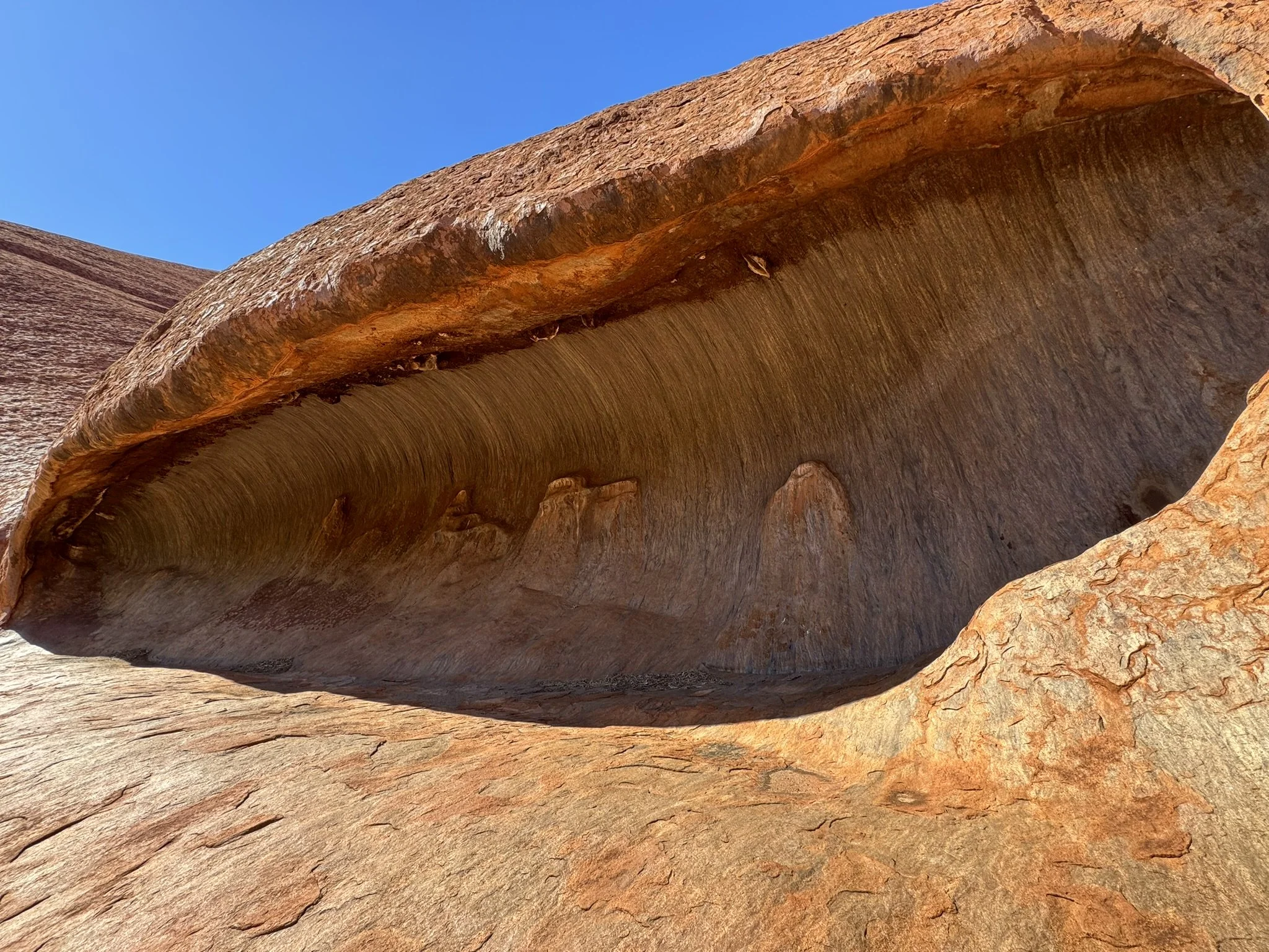 Close-up of a smooth, reddish-brown rock formation with a large hollow, under a clear blue sky.