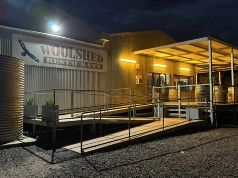 Exterior of Woolshed Restaurant at night with a ramp leading to the entrance, illuminated by outdoor lighting.
