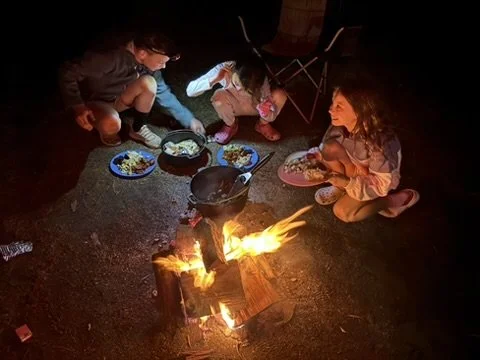 Children sitting around a campfire eating food at night.