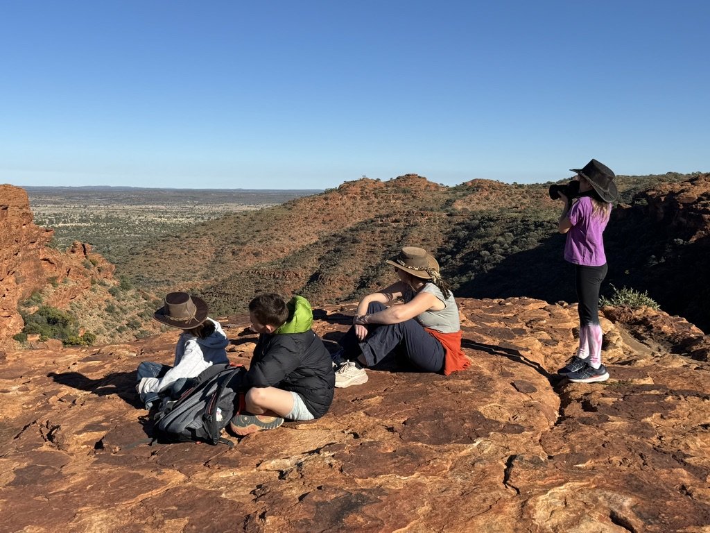 Four children sitting and standing on a rocky ledge overlooking a desert canyon landscape.