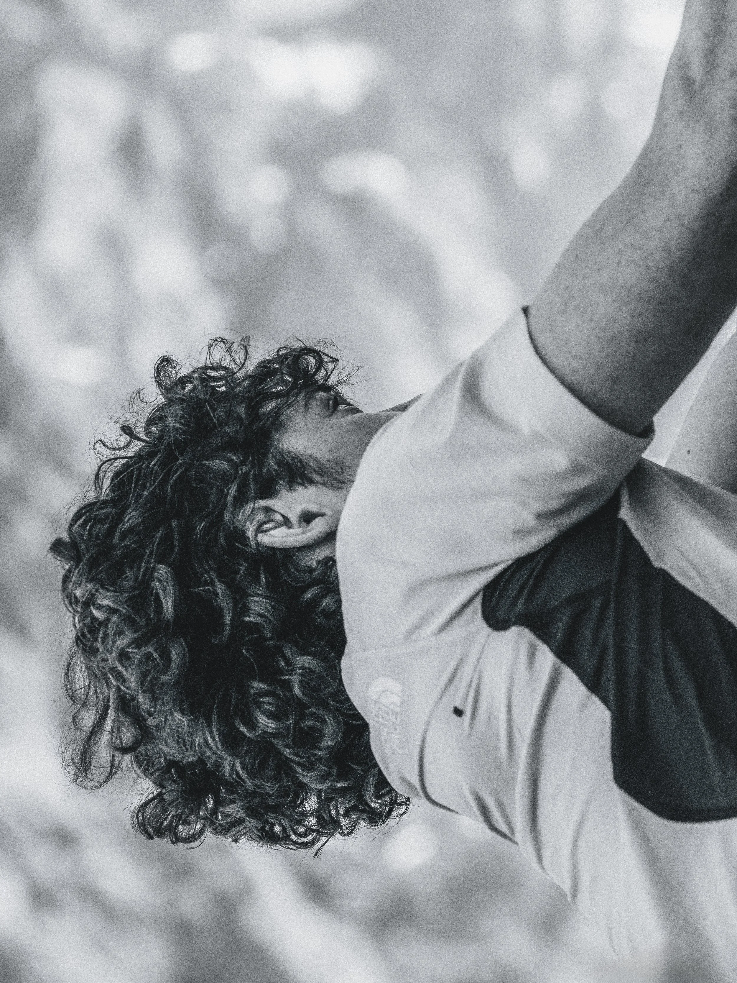 A man with curly hair wearing a jacket, seen from below, looking upwards with a blurred background.