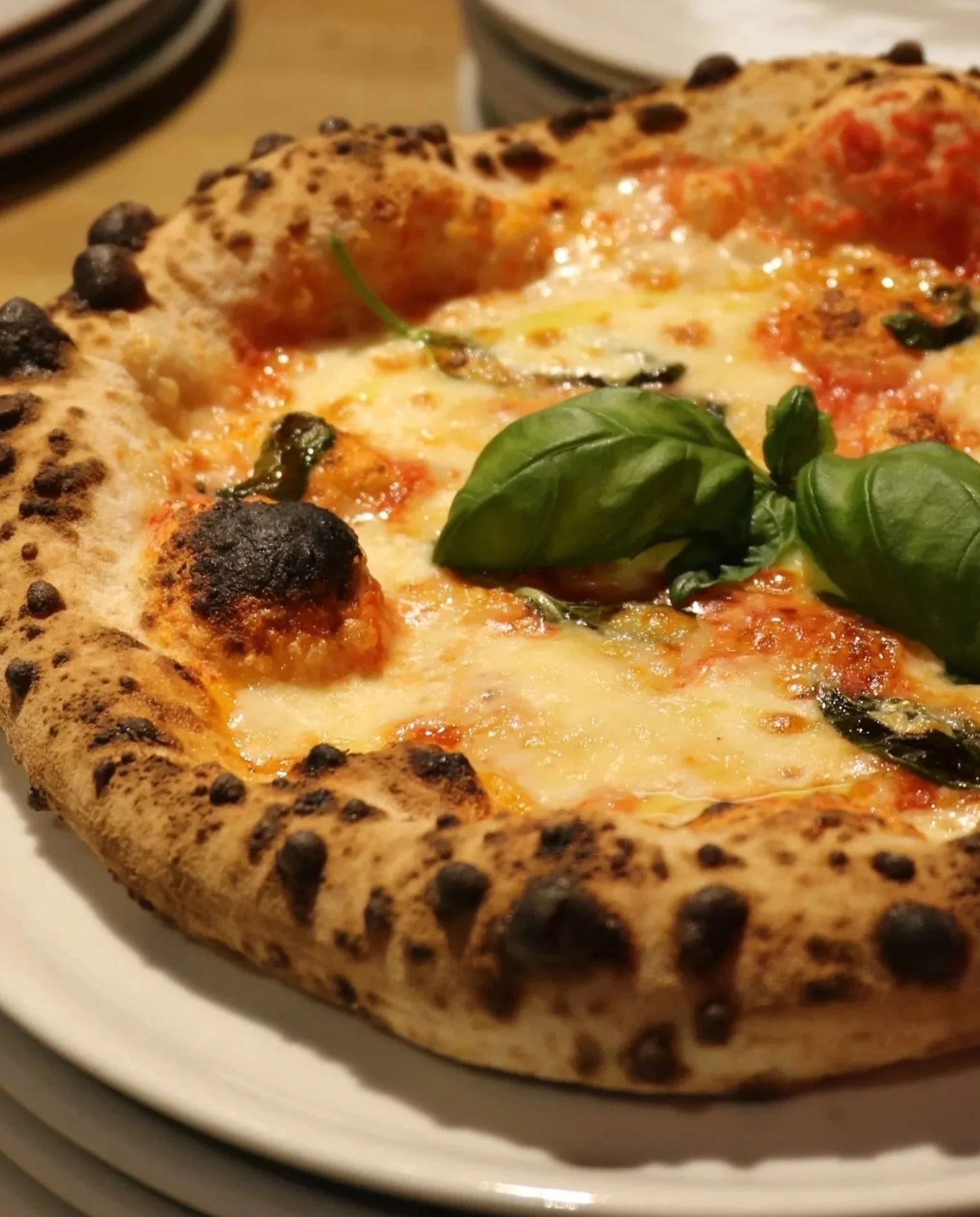 Close-up of a margherita pizza with melted cheese, tomato sauce, and fresh basil leaves on top, served on a white plate.
Nærbilde av en margherita pizza med smeltet ost, tomatsaus på San Marzano tomater og ferske basilikumblader på toppen.