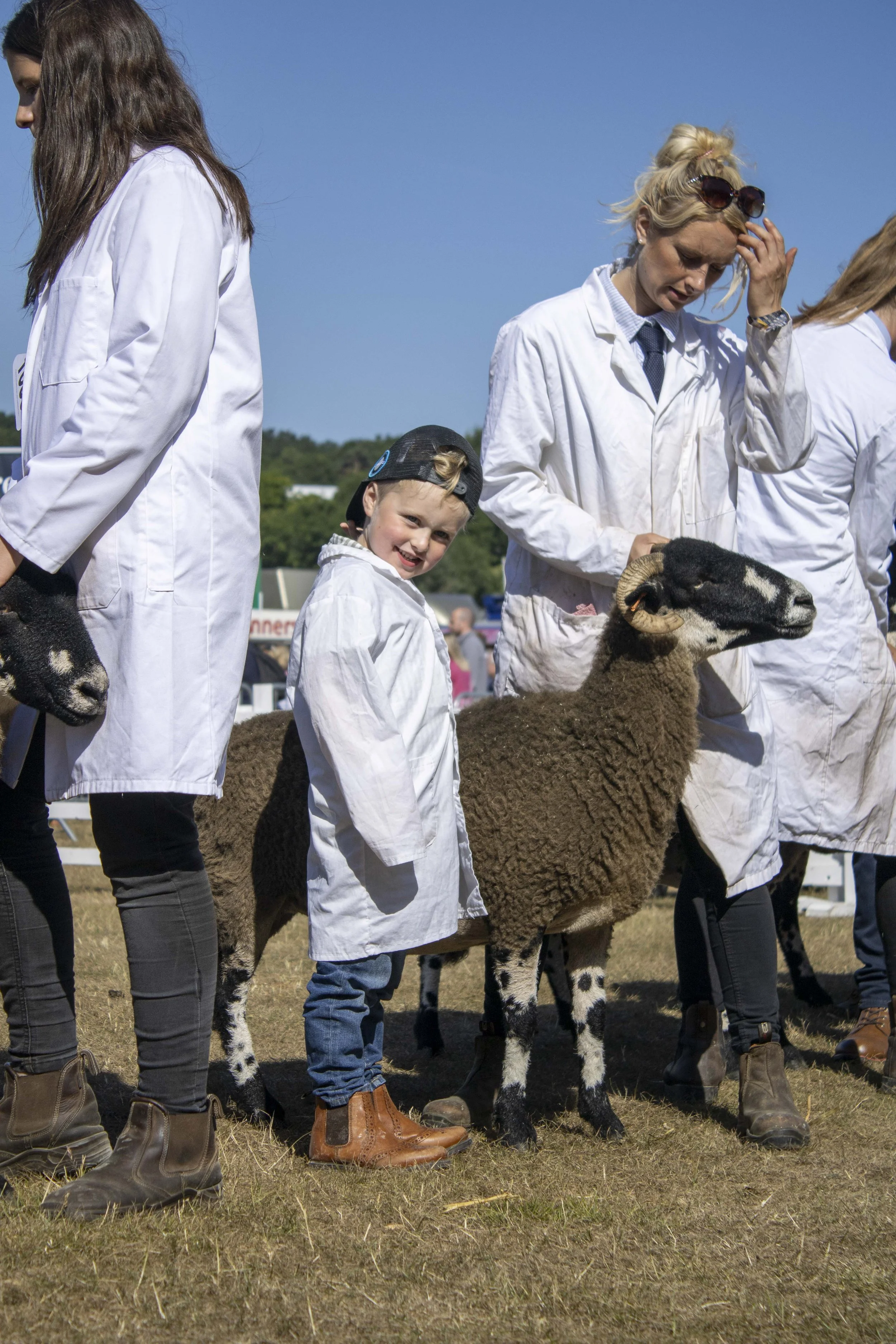Children and adults in white coats at a farm event, with a sheep and a kid smiling.