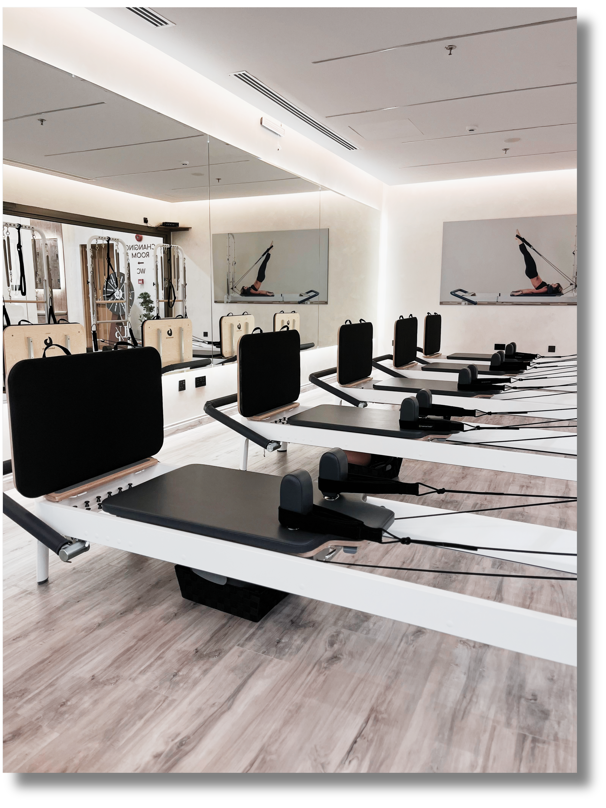 Pilates reformer machines in a modern fitness studio with large mirror, framed wall art, and light wood flooring.
