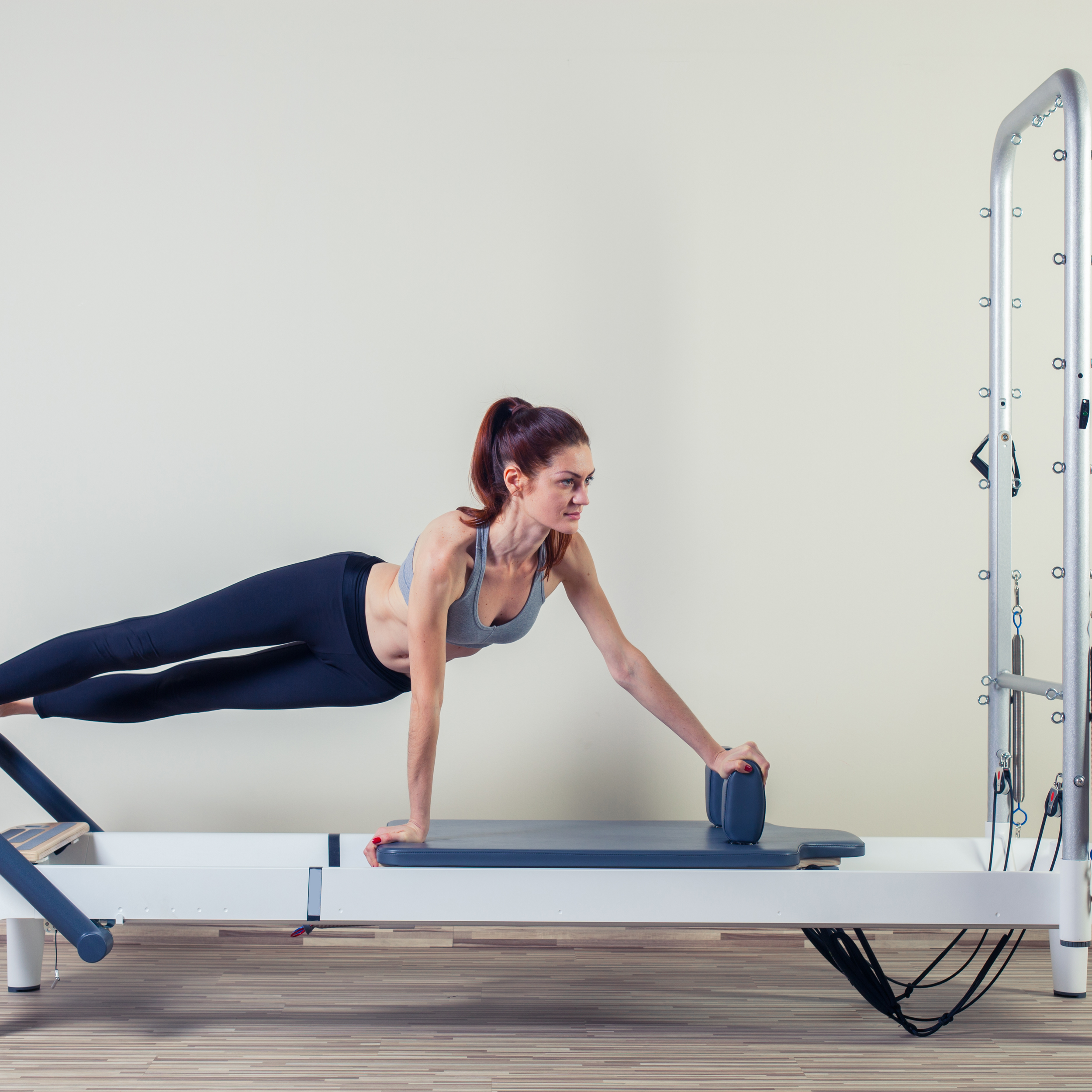 Woman performing a side plank exercise on a Pilates reformer machine in a gym.