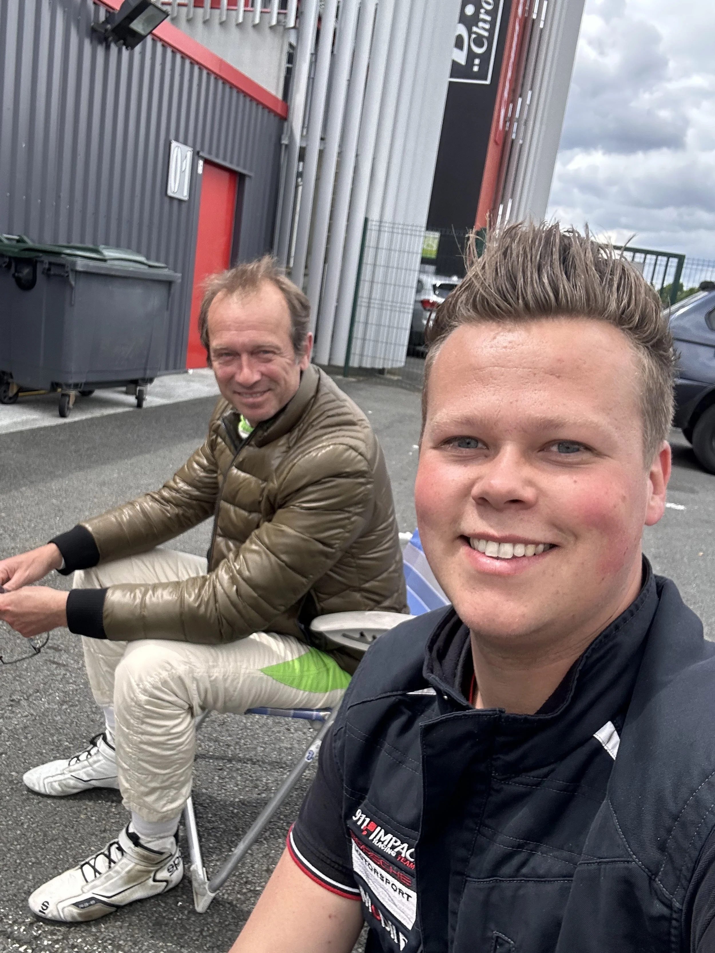 Deux hommes prennent un selfie devant un bâtiment industriel ou commercial, l'homme en première plan souriant est pierre malderez de la societe malderez , la scène ce passe au circuit de Mettet