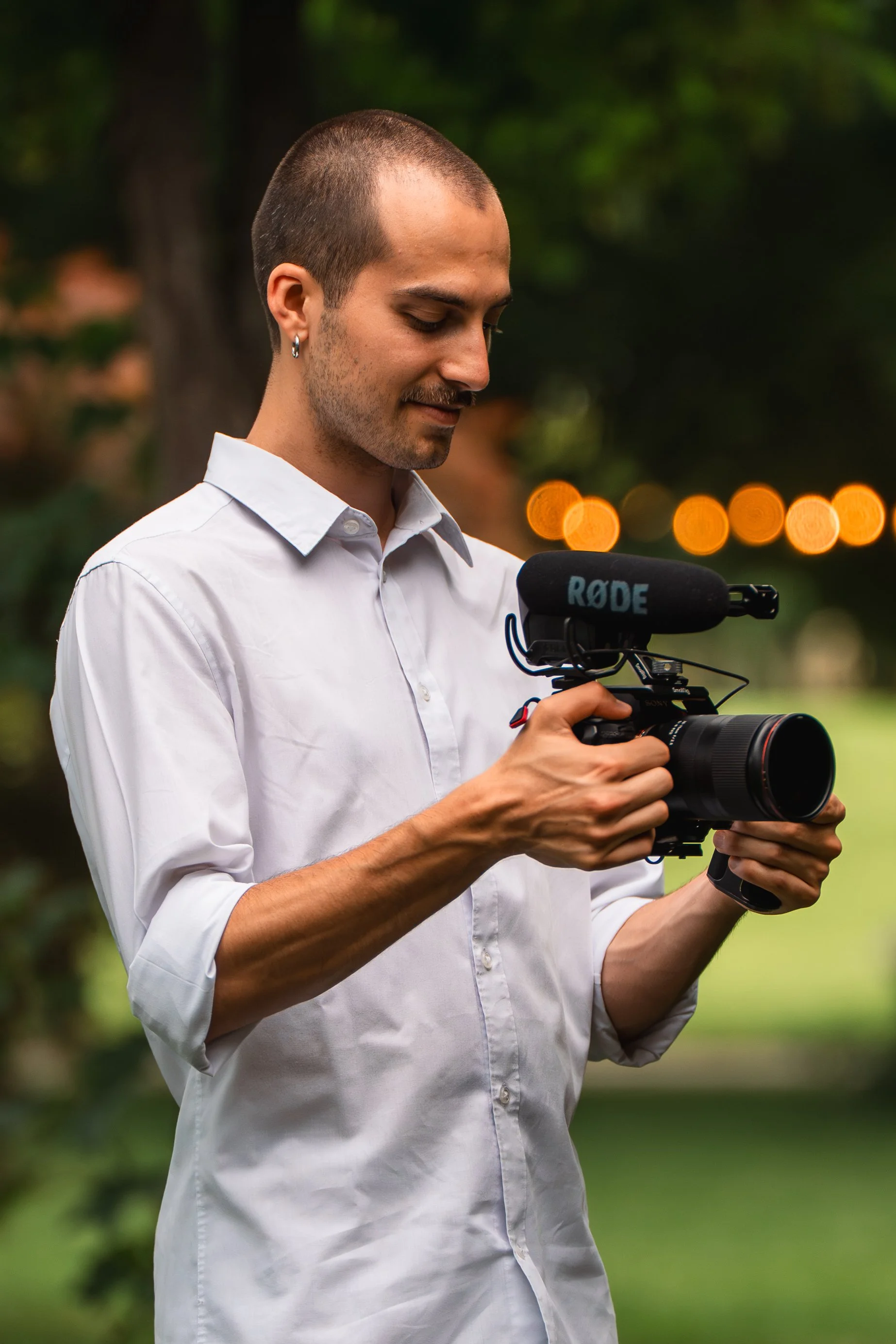Uomo con camicia bianca che tiene una videocamera con microfono RODE nel parco di una villa.