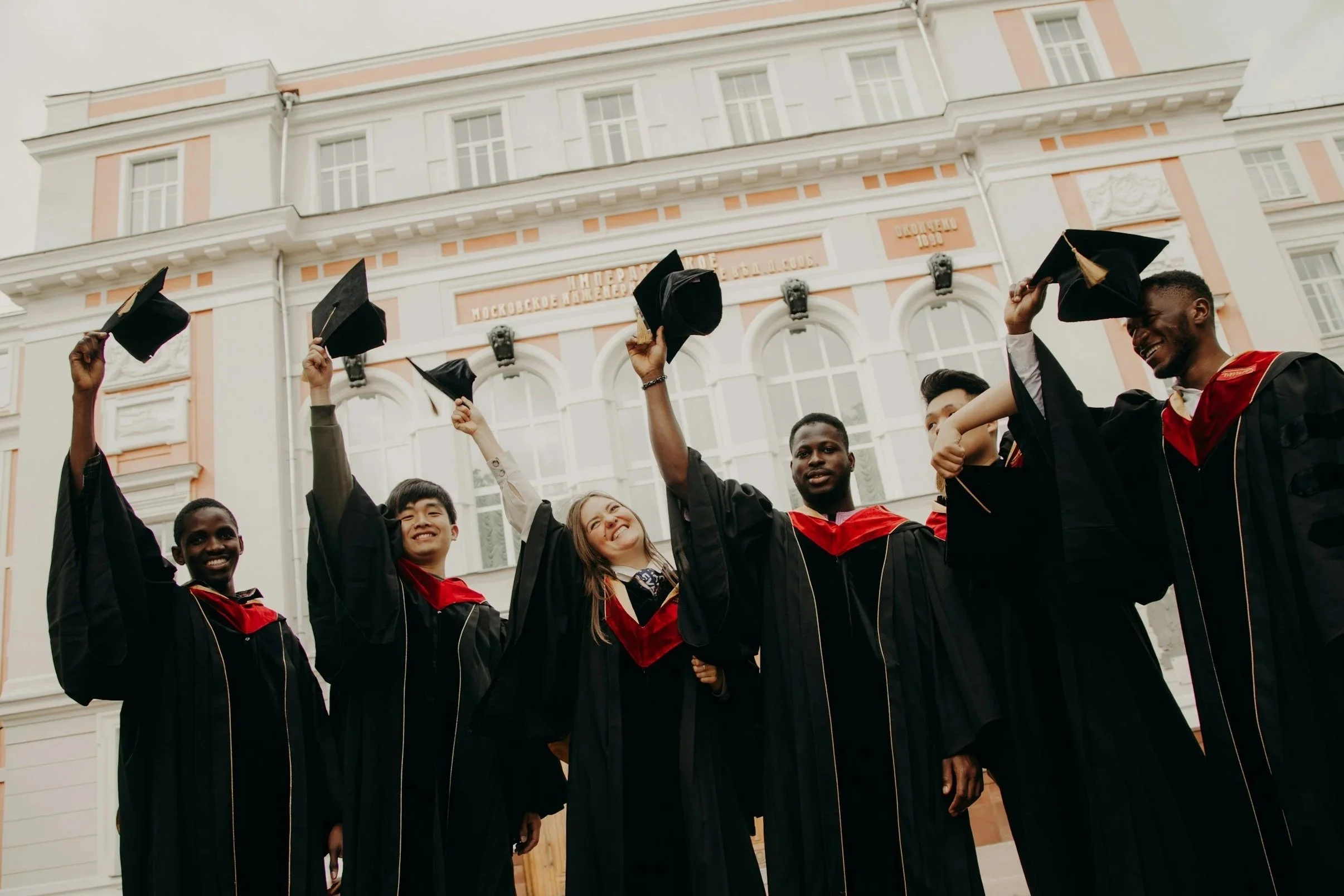 Group of diverse students in graduation gowns and caps celebrating outdoors