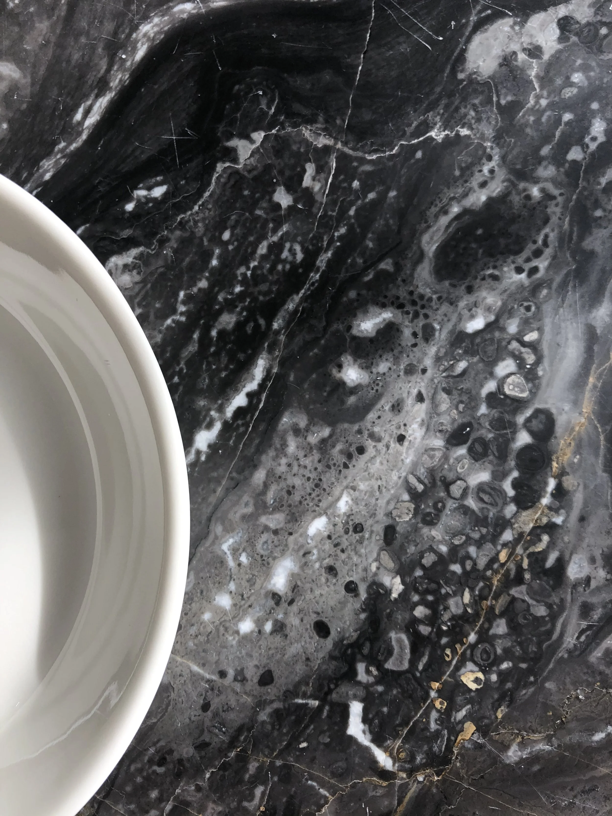 Part of a white plate on a black marble countertop with white and gray veining and bubbles.