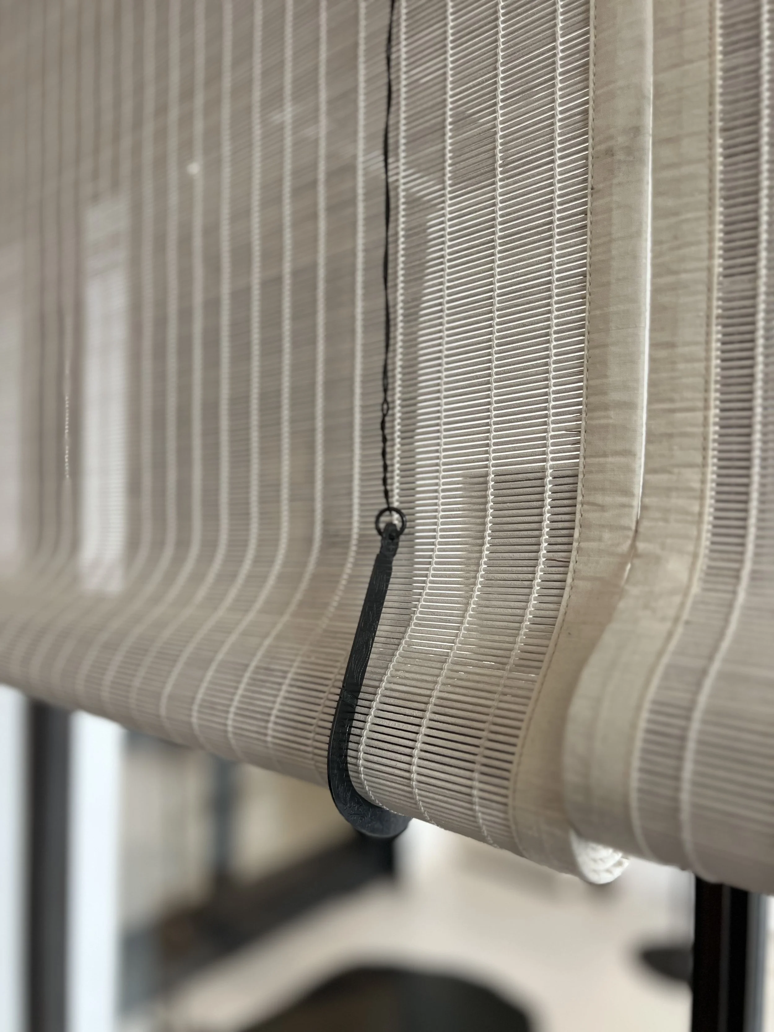 Close-up of a beige bamboo window shade with a black pull cord hanging in the center.