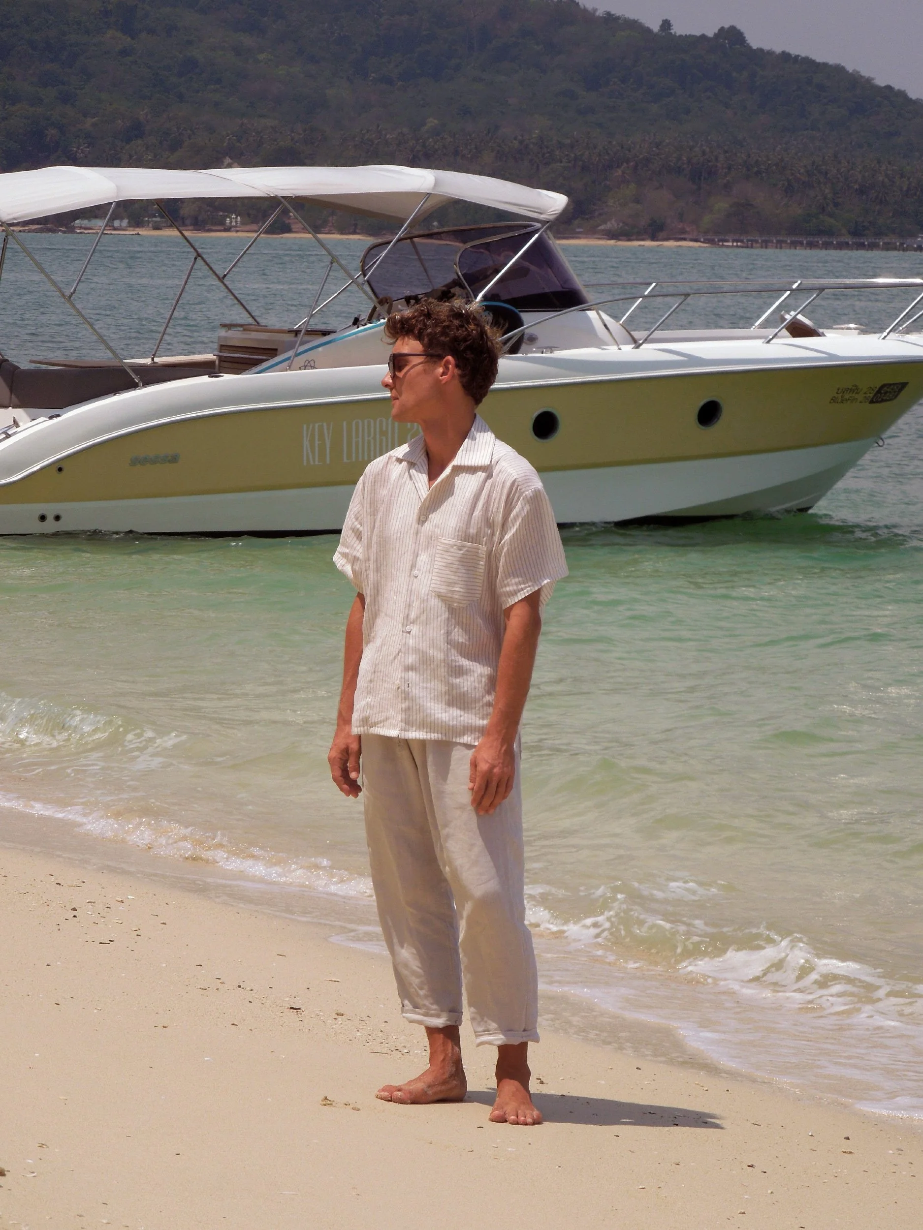 model wearing beige shirt on the beach in front of a boat