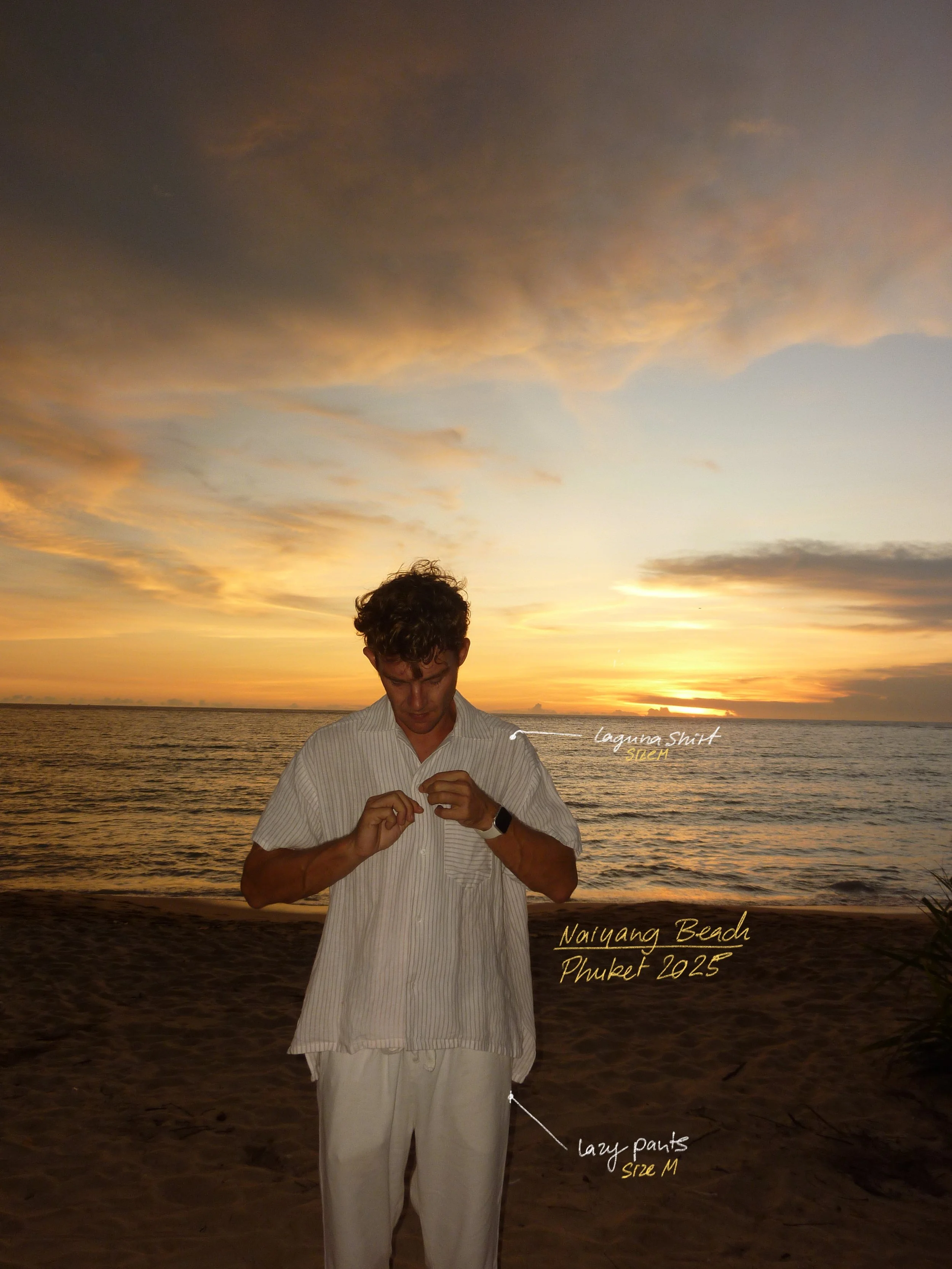 A man wearing a light-colored striped shirt and loose white pants standing on a beach during sunset, with writing pointing out details like a Laguna shirt, Naiyang Beach in Phuket 2025, and loose pants size M.