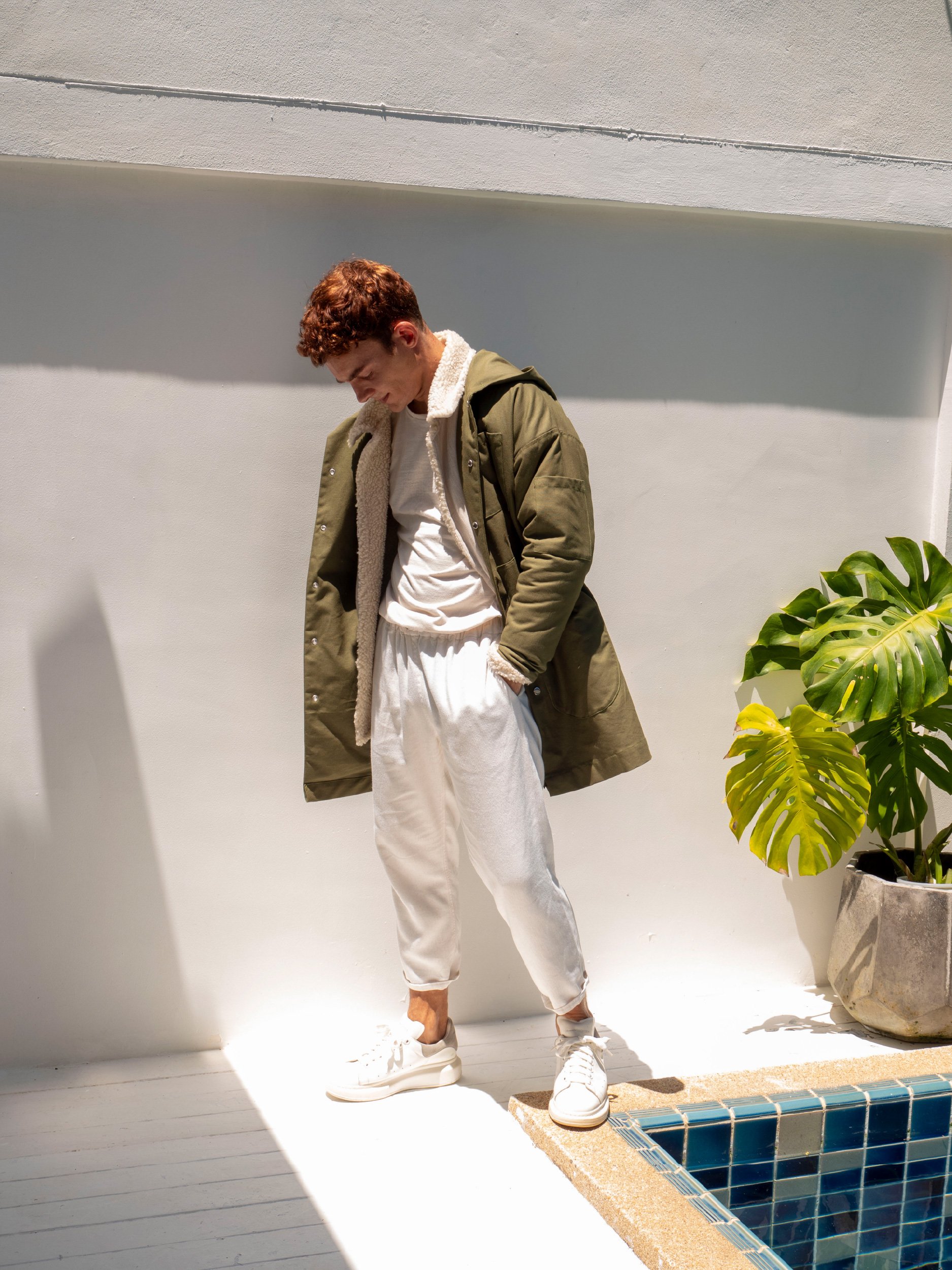 model wearing long green boxy parka with hood layered over beige jacket version