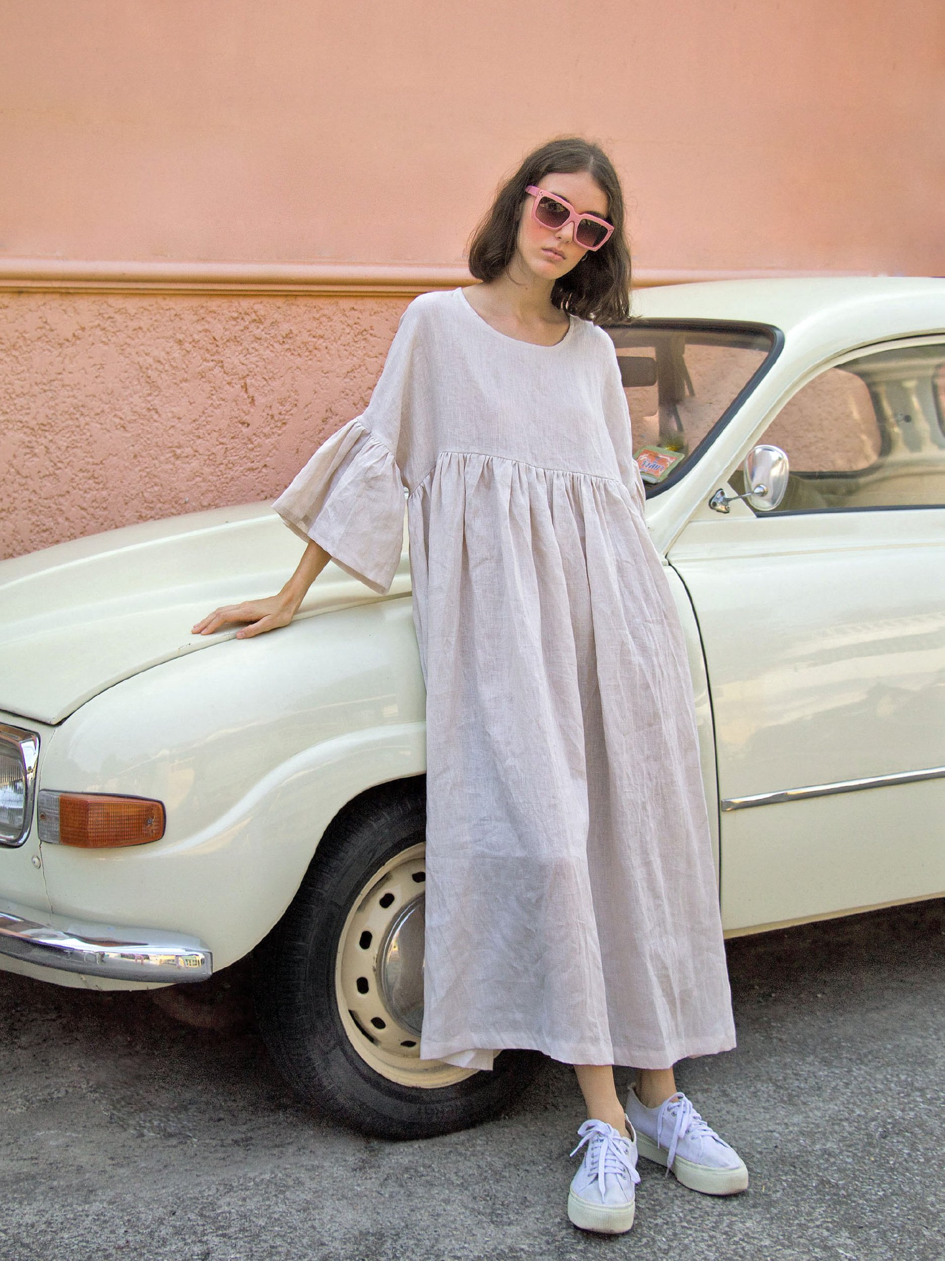 model wearing aria dress casually leaning against classic yellow car infront of a soft orange wall