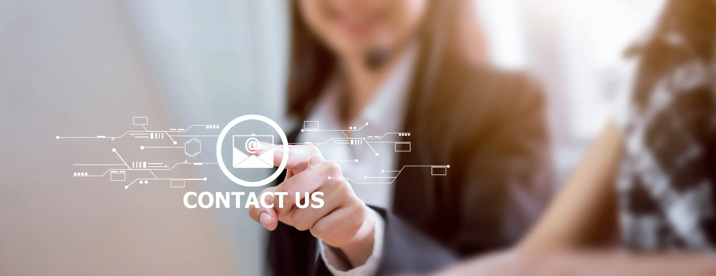 A woman in business attire points at a virtual contact us icon, with digital graphics and circuits around her finger.
